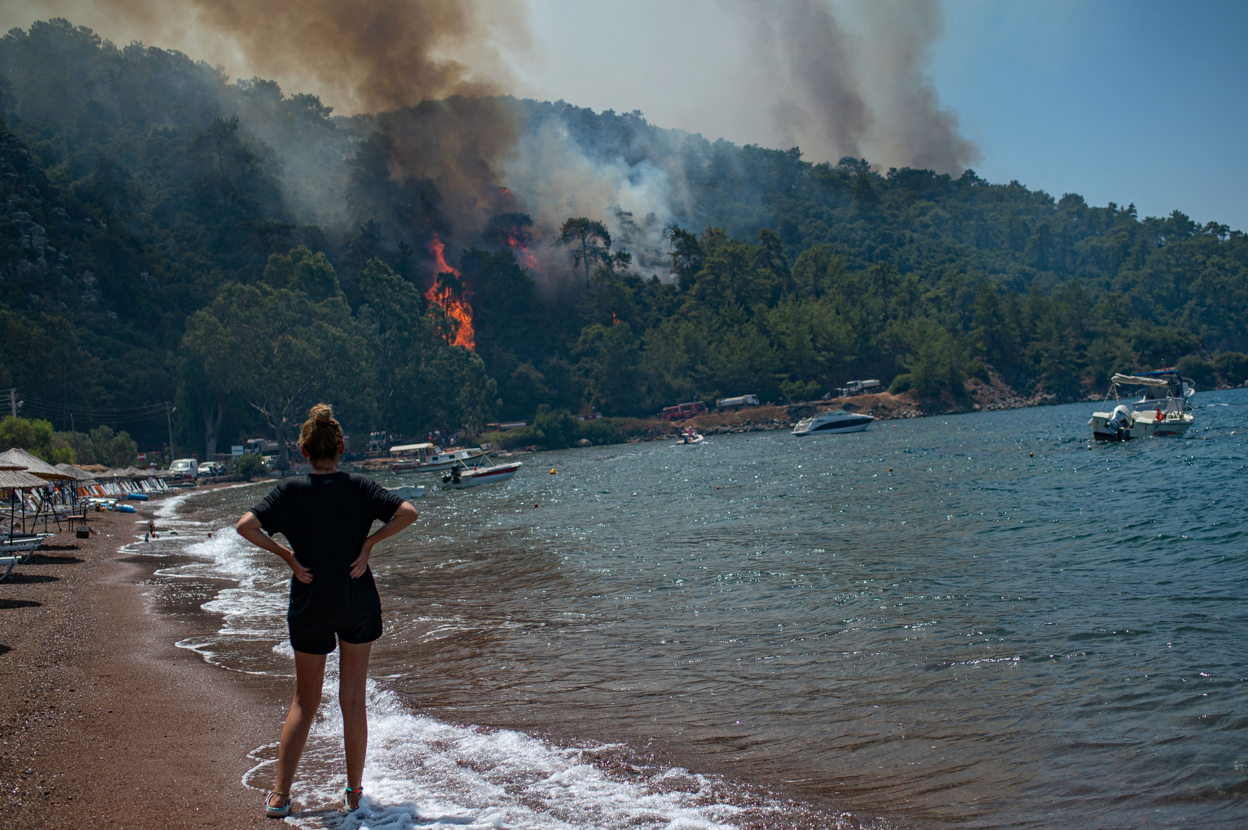 A woman standing on a beach watches the forest burning in Mugla, Turkey