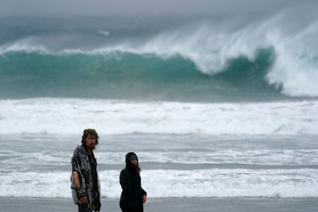 <p>People walk along Mission Beach as large waves pound the area on Tuesday in San Diego. Rain is drenching Southern California as a powerful storm slides down the state</p>