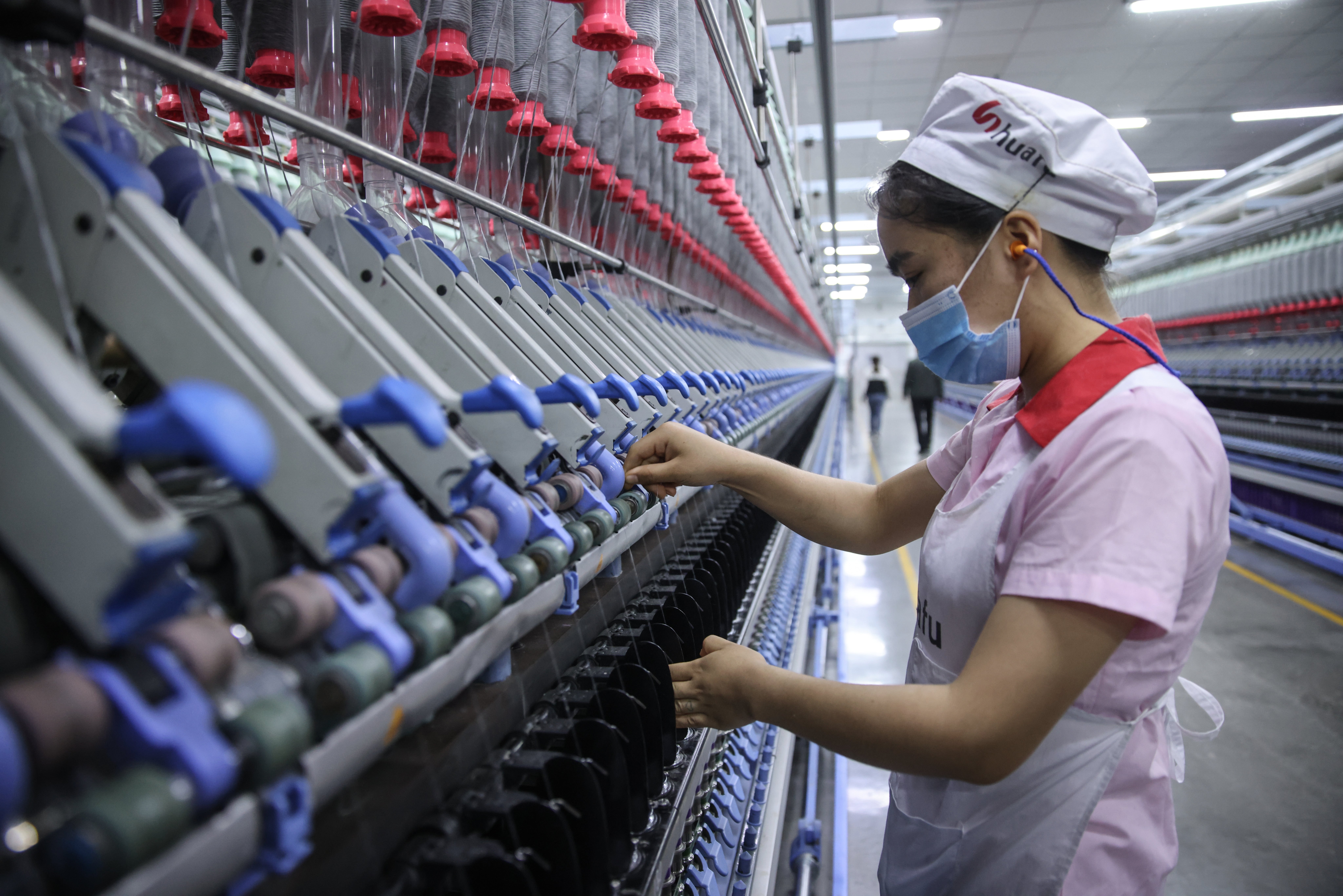 An ethnic minority worker operates cotton yarn machinery in a textile factory in Xinjiang, China