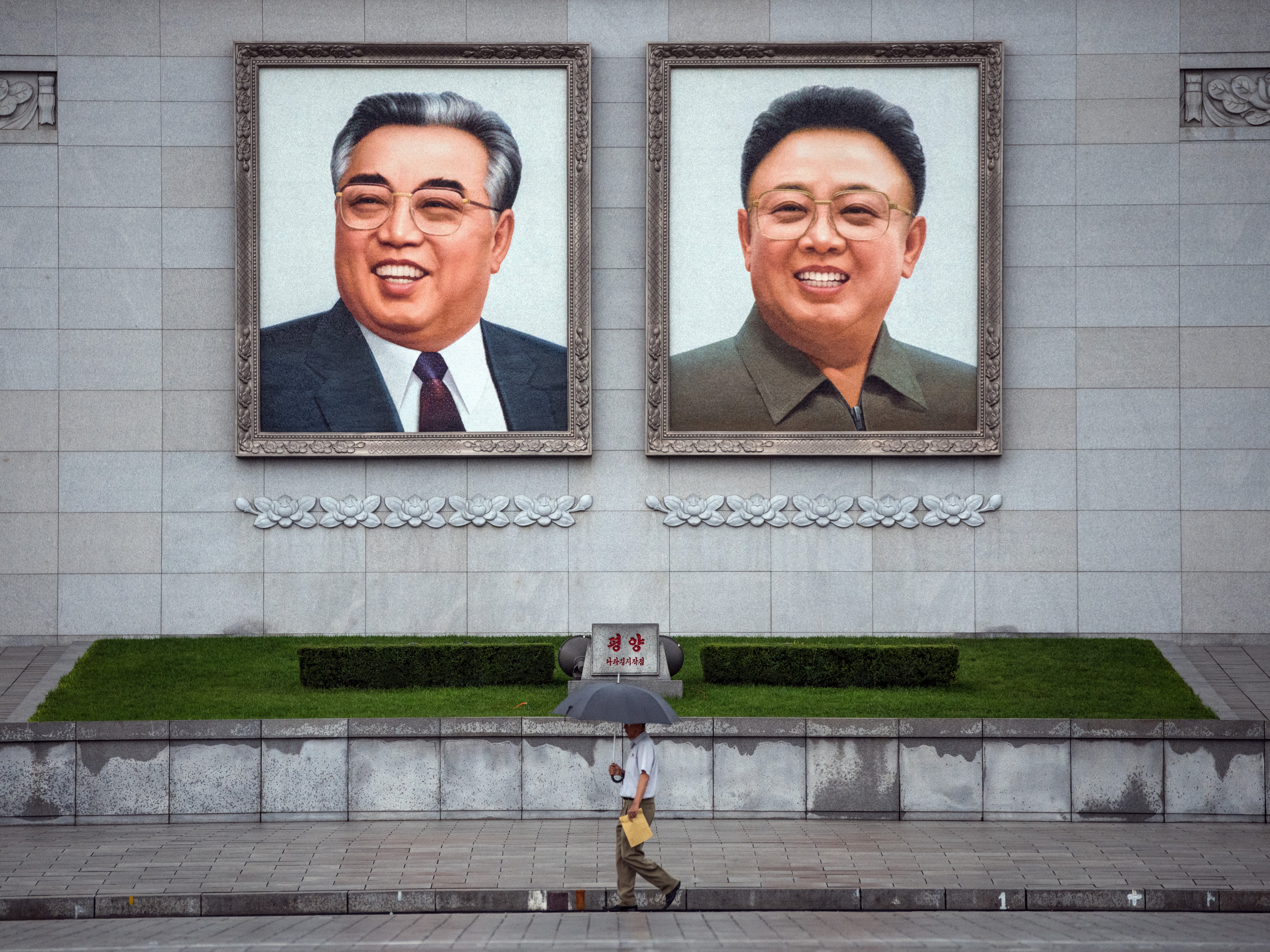 File: People walk beneath huge pictures of Kim Il-sung and Kim Jong-il displayed from the Parade Reviewing Stand in Kim il-Sung Square, on 23 August 2018 in Pyongyang, North Korea