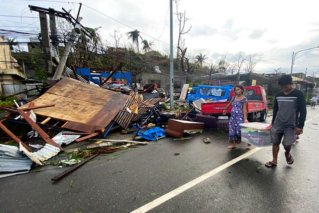 <p>Residents carry what's left of their belongings as they walk past damaged homes due to Typhoon Rai in Surigao city</p>