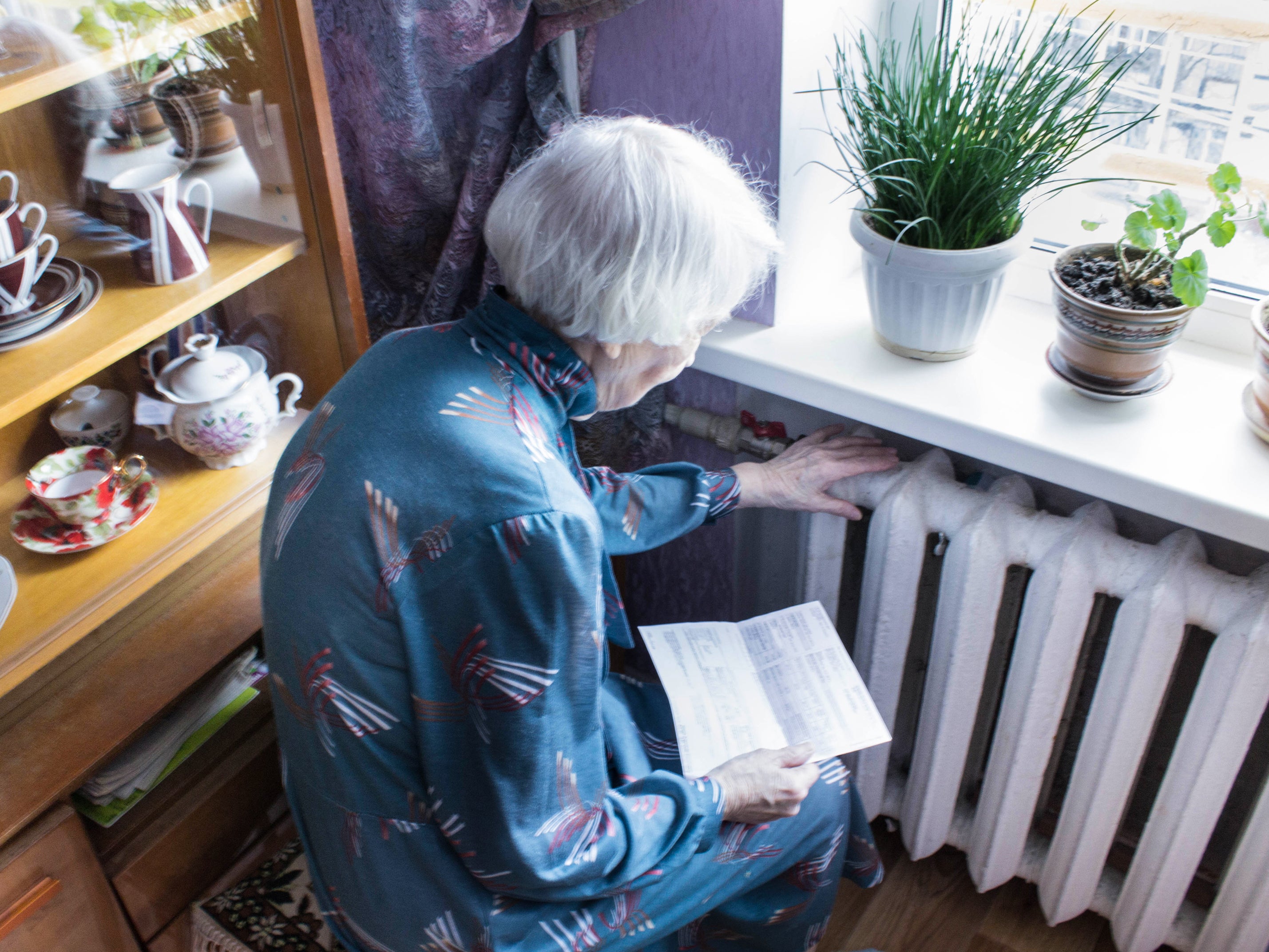 An older woman holding energy bill in front of a radiator