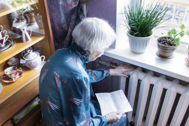 <p>An older woman holding energy bill in front of a radiator</p>