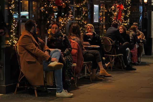 People sit on outdoor tables outside a restaurant on Old Compton Street in Soho, London (Kirsty O’Connor/PA)