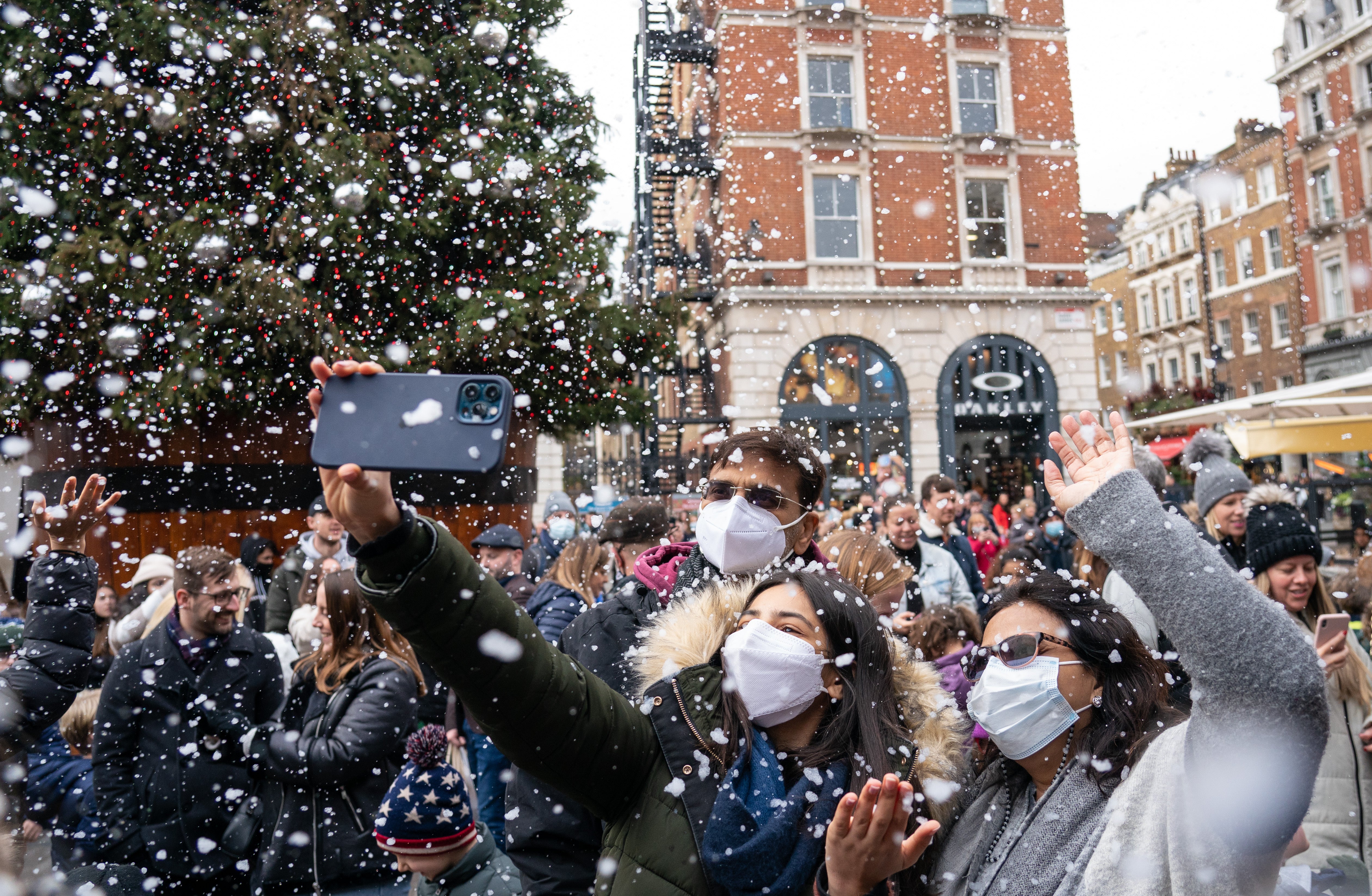 People wearing face masks enjoy a shower of artificial snow in Covent Garden, London, as the government refused to rule out introducing further restrictions to slow the spread of the Omicron variant of coronavirus (PA)