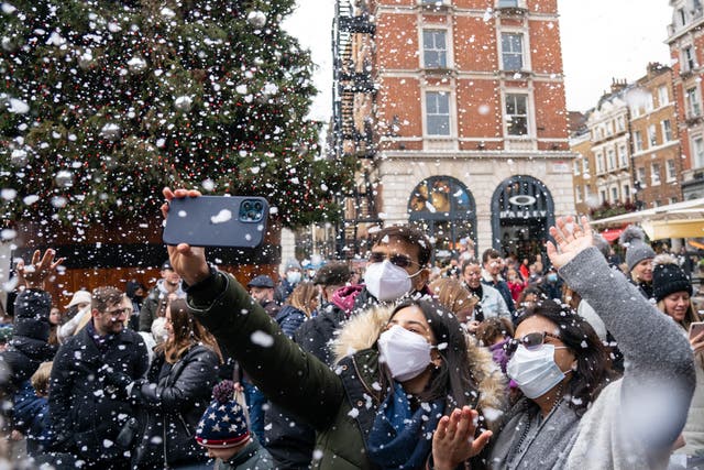 People wearing face masks enjoy a shower of artificial snow in Covent Garden, London, as the government refused to rule out introducing further restrictions to slow the spread of the Omicron variant of coronavirus (PA)