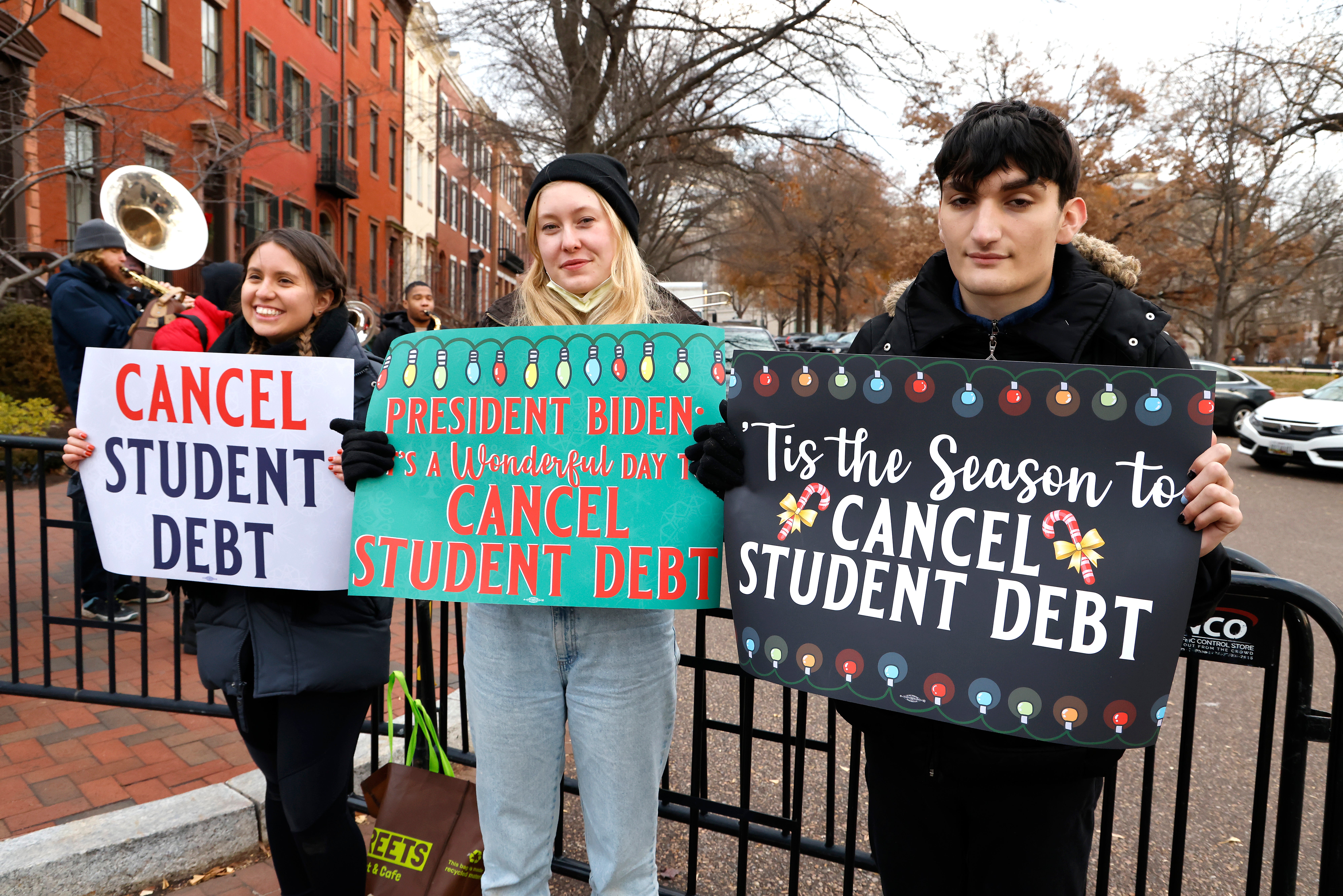 Activists hold festive signs calling on President Biden to cancel student debt and not resume student loan debt while musicians play joyful music, greeting the White House staff as they arrive to work on December 15, 2021 in Washington, DC.