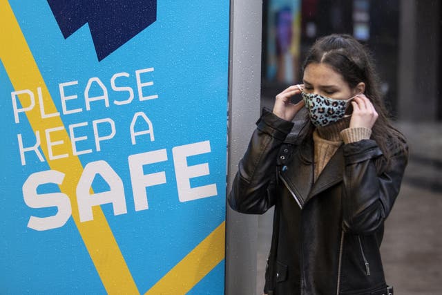 A young woman in Belfast puts on her face covering as she walks past a Covid-19 safety message from Belfast city council (Liam McBurney/PA)