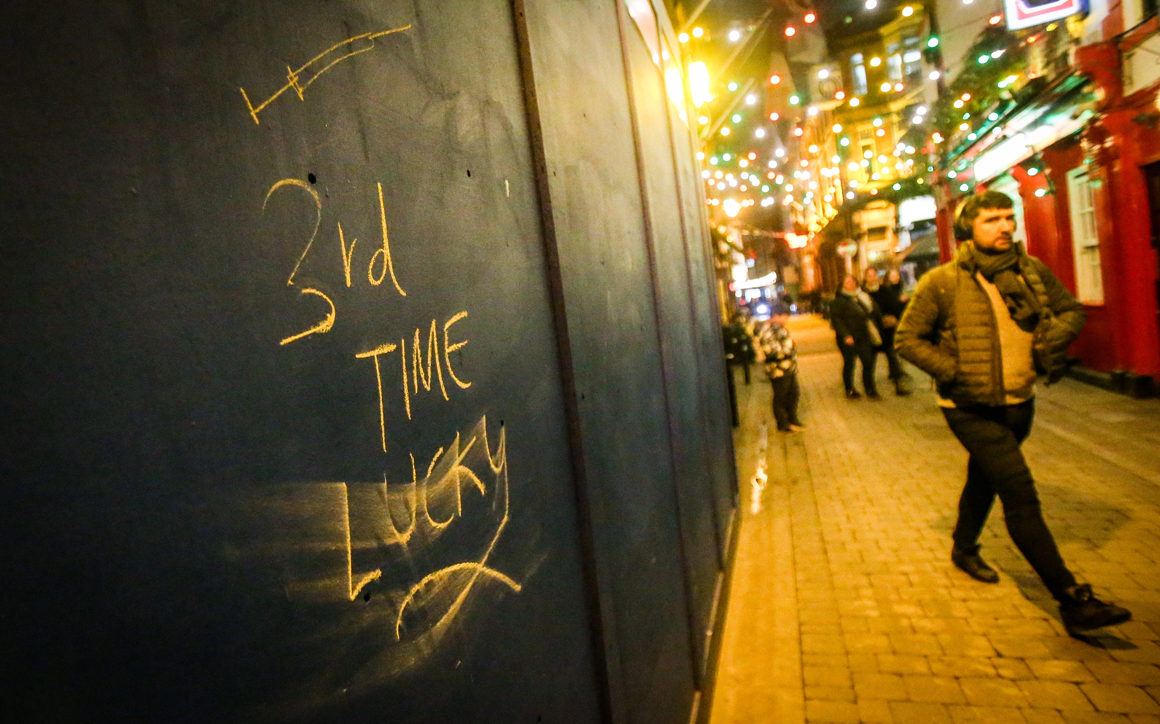 A man walks past Covid vaccine graffiti in Dublin this evening, ahead of a new 8pm closing time for pubs and restaurants in Ireland (Damien Storan/PA)