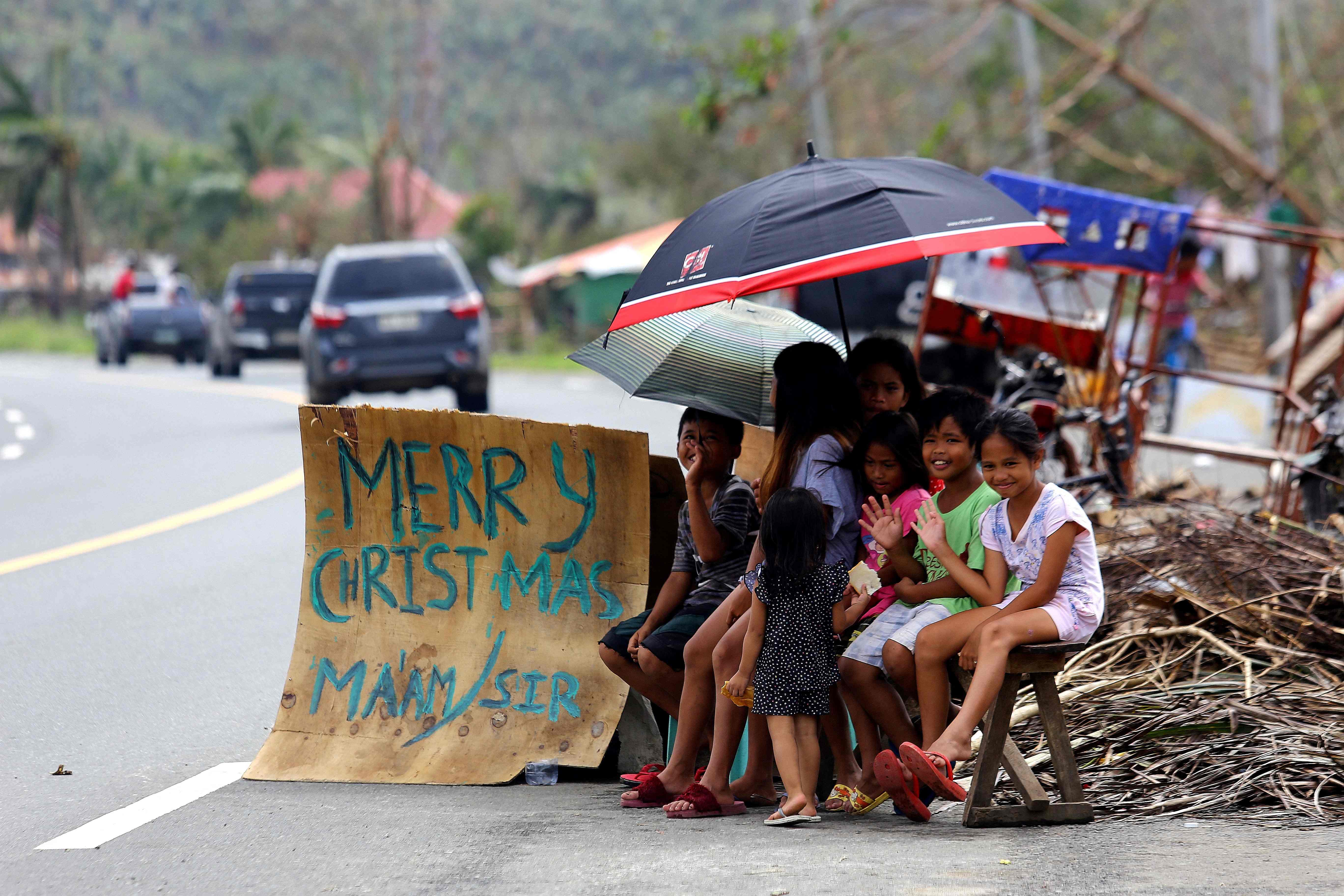 Children display a sign with Christmas greetings as they ask for alms following Typhoon Rai in Surigao City, Philippines, 25 December 2021