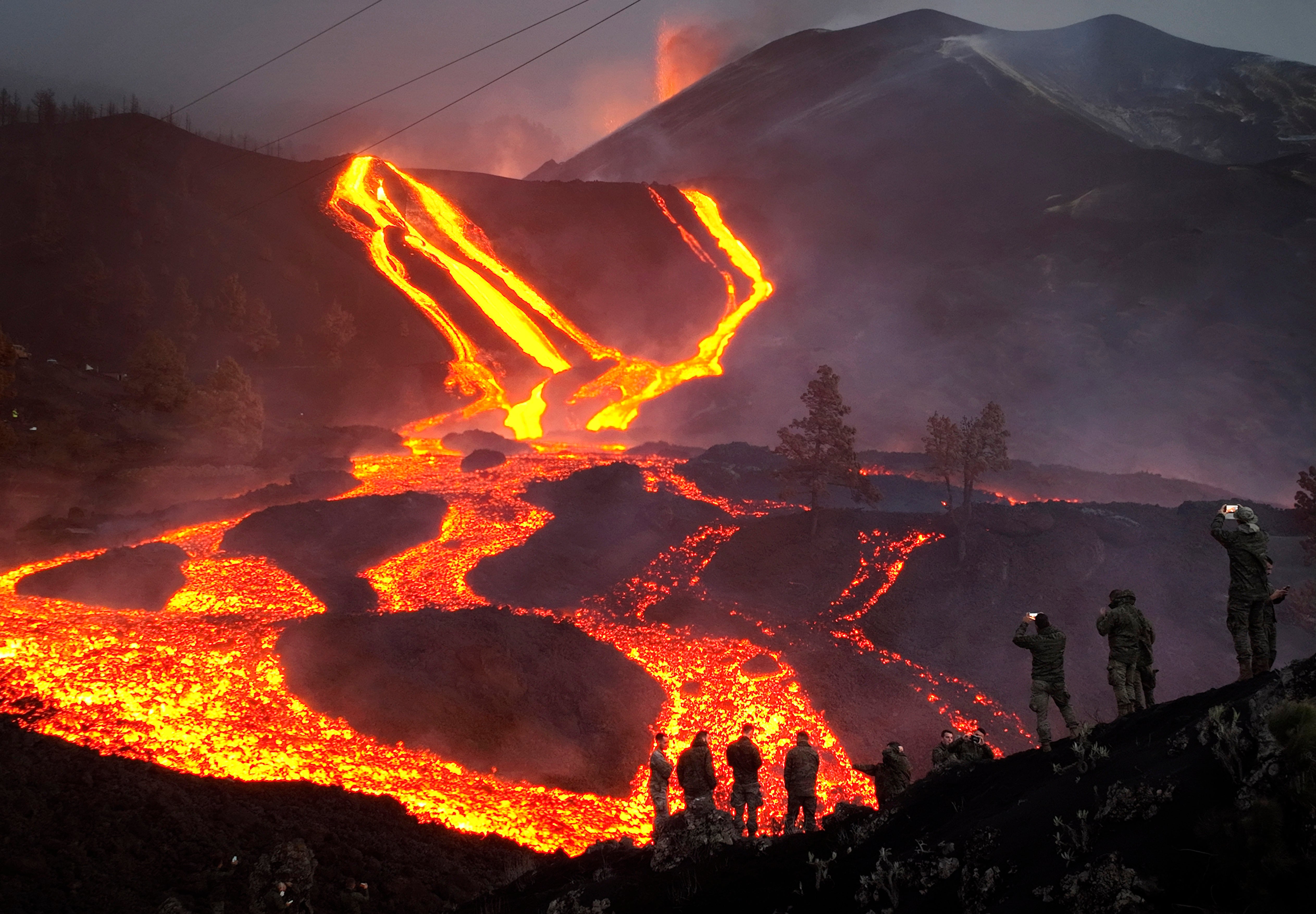 Spanish Army soldiers stand on a hill as lava flows on the Canary island of La Palma in November