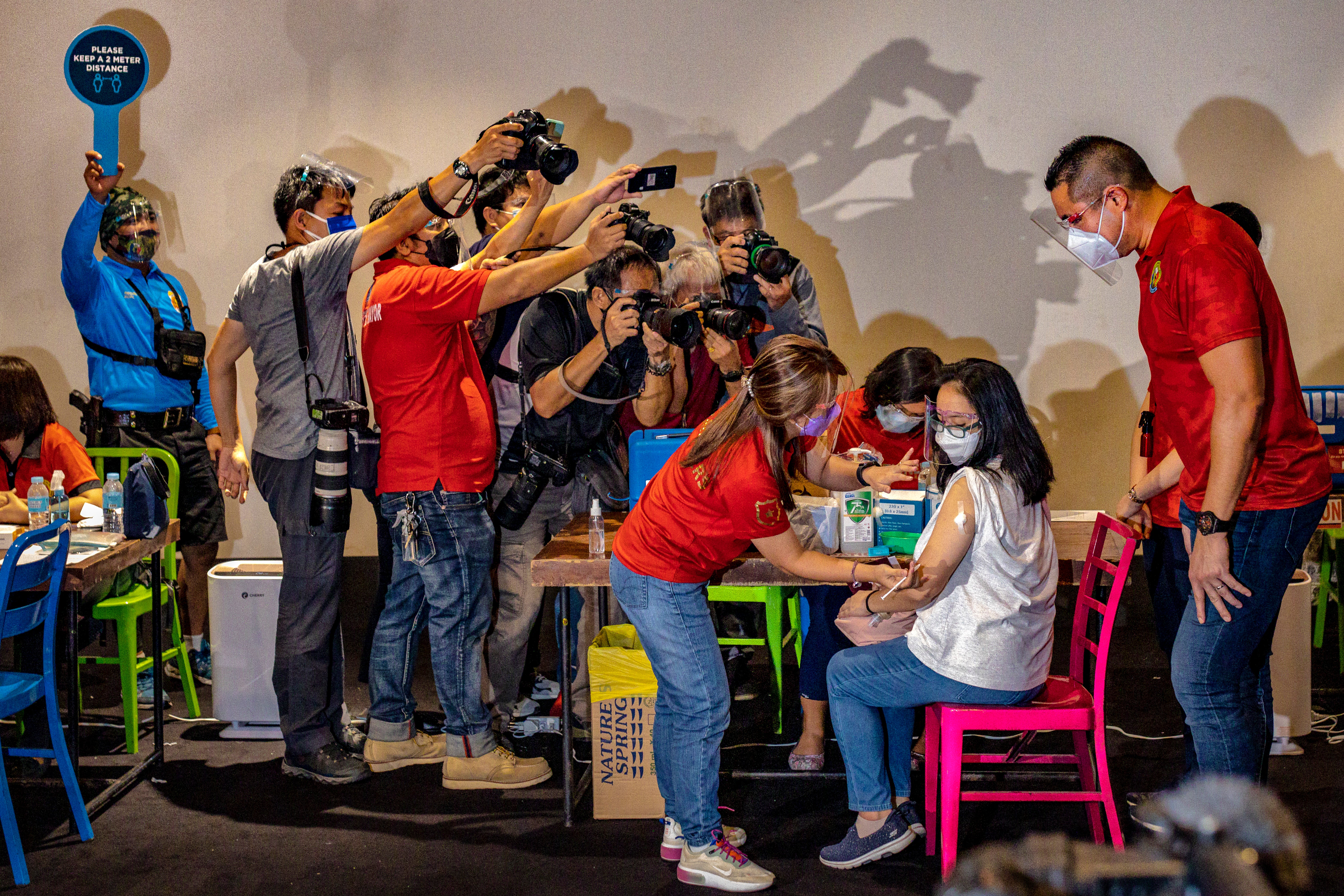 Members of the media take pictures as a healthcare worker administers a Covid vaccine to a woman in San Juan, Philippines