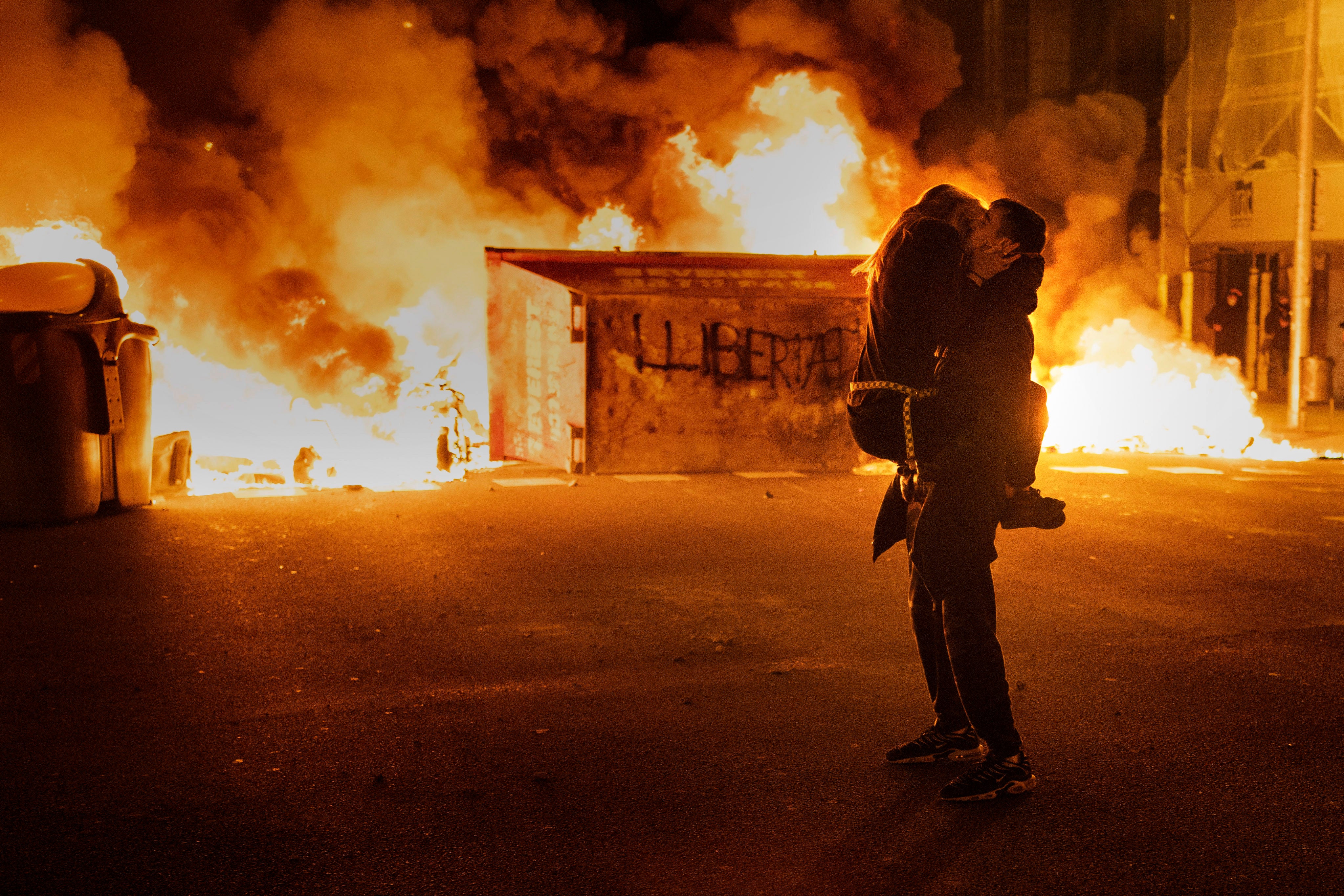 A couple kiss in front of a barricade set on fire by demonstrators during clashes with police following a protest condemning the imprisonment of rap singer Pablo Hasél in Barcelona, Spain