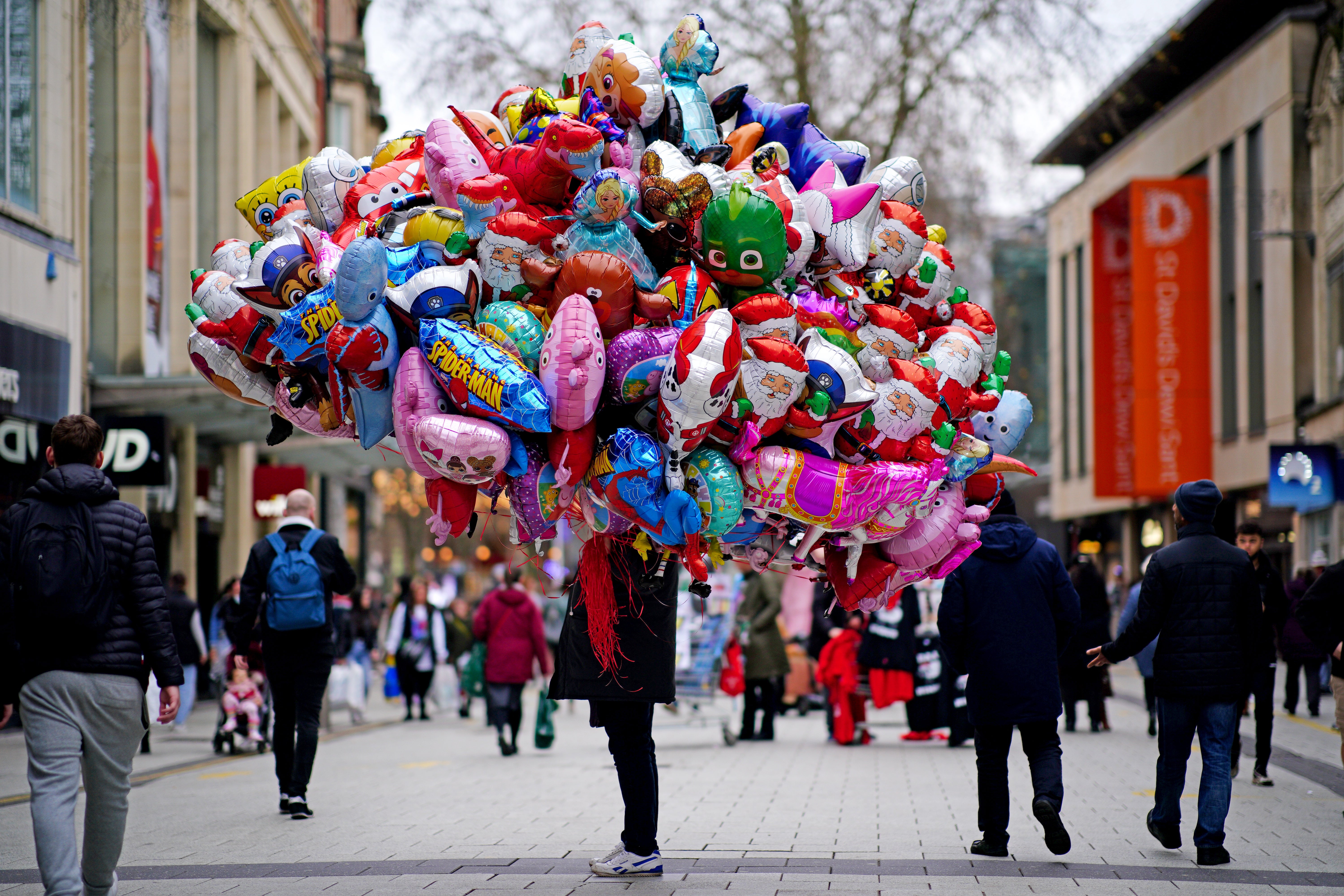 A balloon vendor is passed by Christmas shoppers in the centre of Cardiff in December (Ben Birchall/PA)