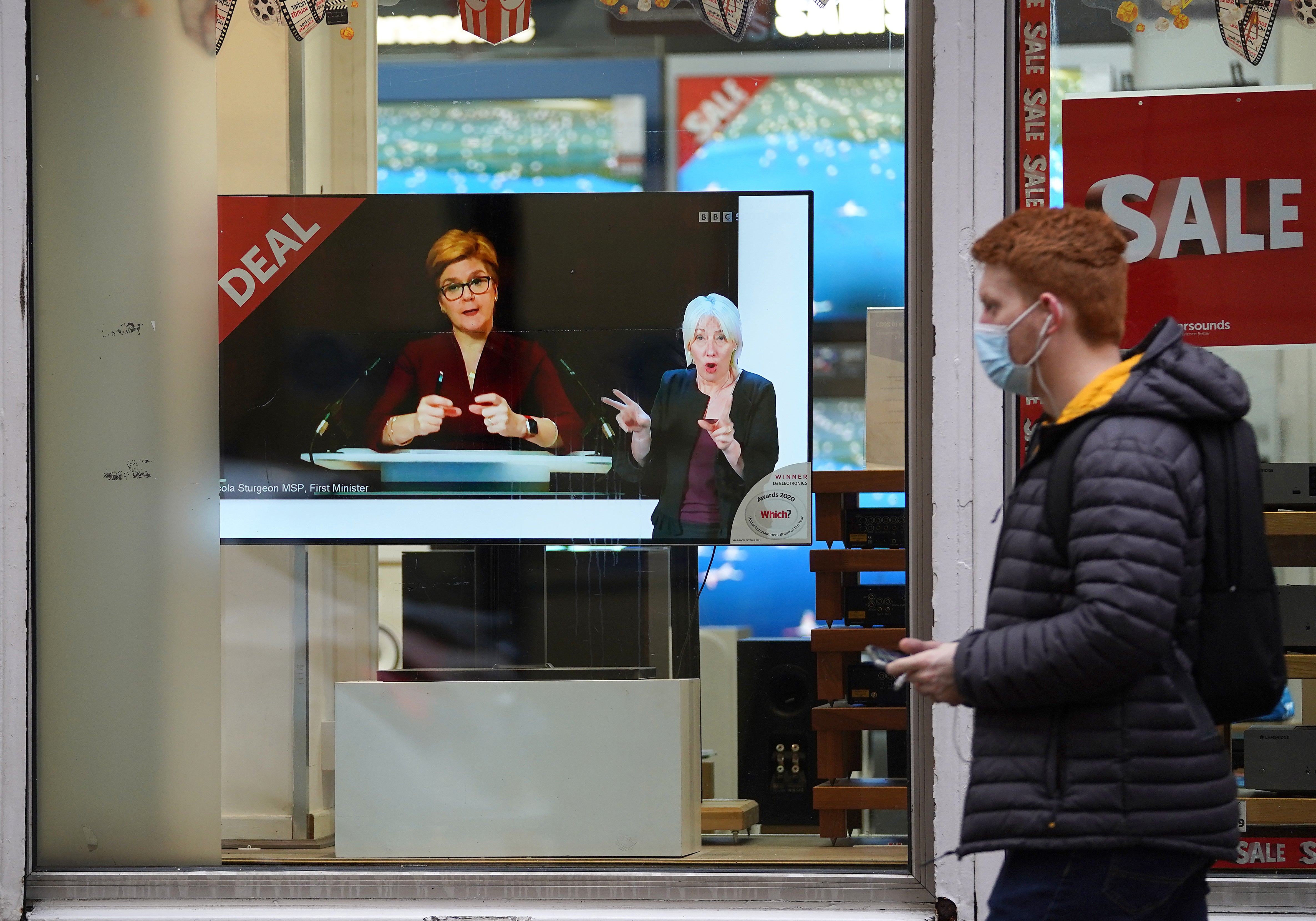 Passers-by look at a TV screen showing First Minister Nicola Sturgeon making a Covid-19 statement (Andrew Milligan/PA)
