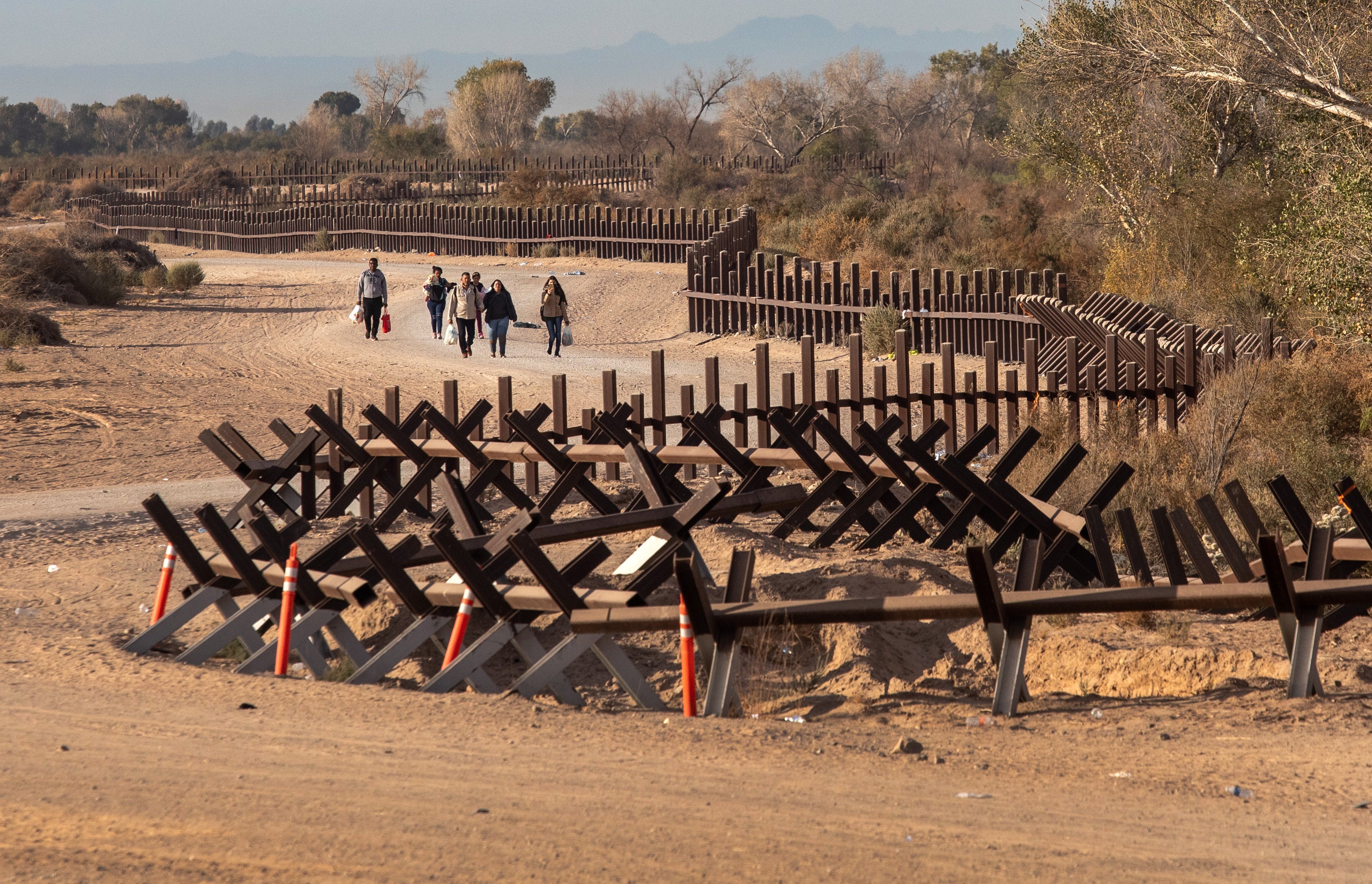 Immigrant families walk after crossing over a vehicle barrier at the US-Mexico border on December 07, 2021 in Yuma, Arizona