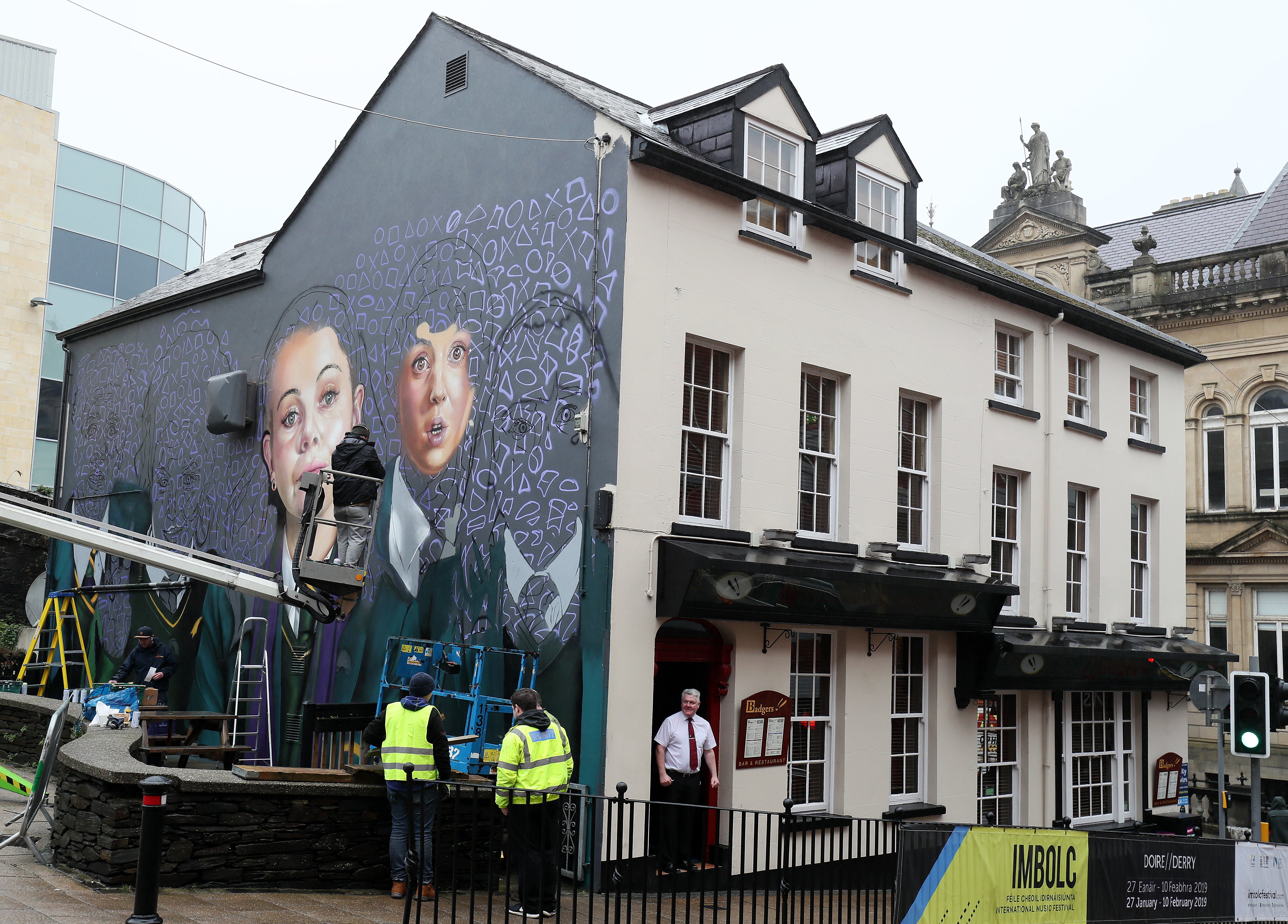 Graffiti artists work on a mural of hit TV show Derry Girls on the wall of Badgers Bar in Orchard Street, Londonderry (Brian Lawless/PA)