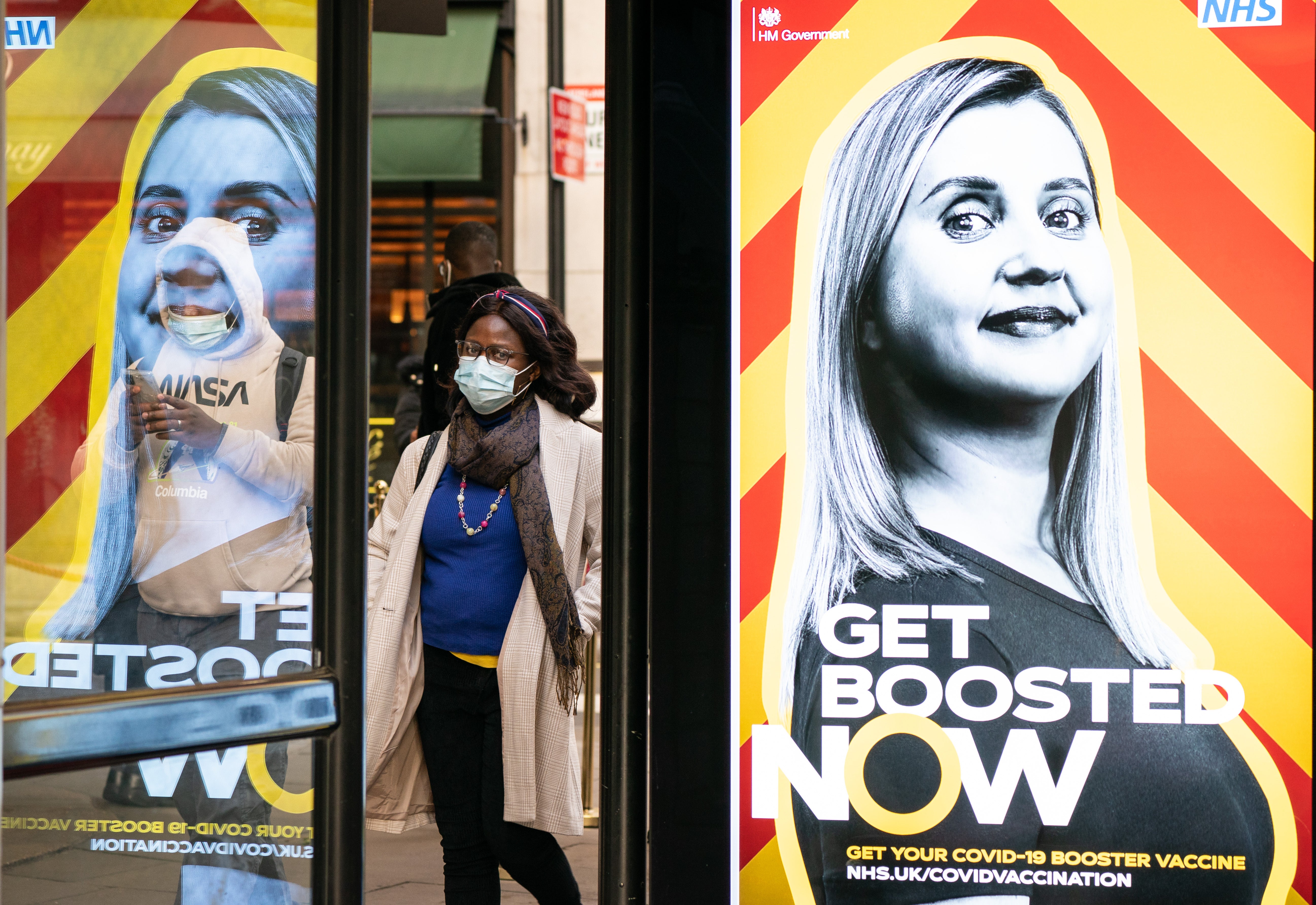 People wearing face masks walk past a UK Government advert encouraging people to book a Covid booster (Dominic Lipinski/PA)