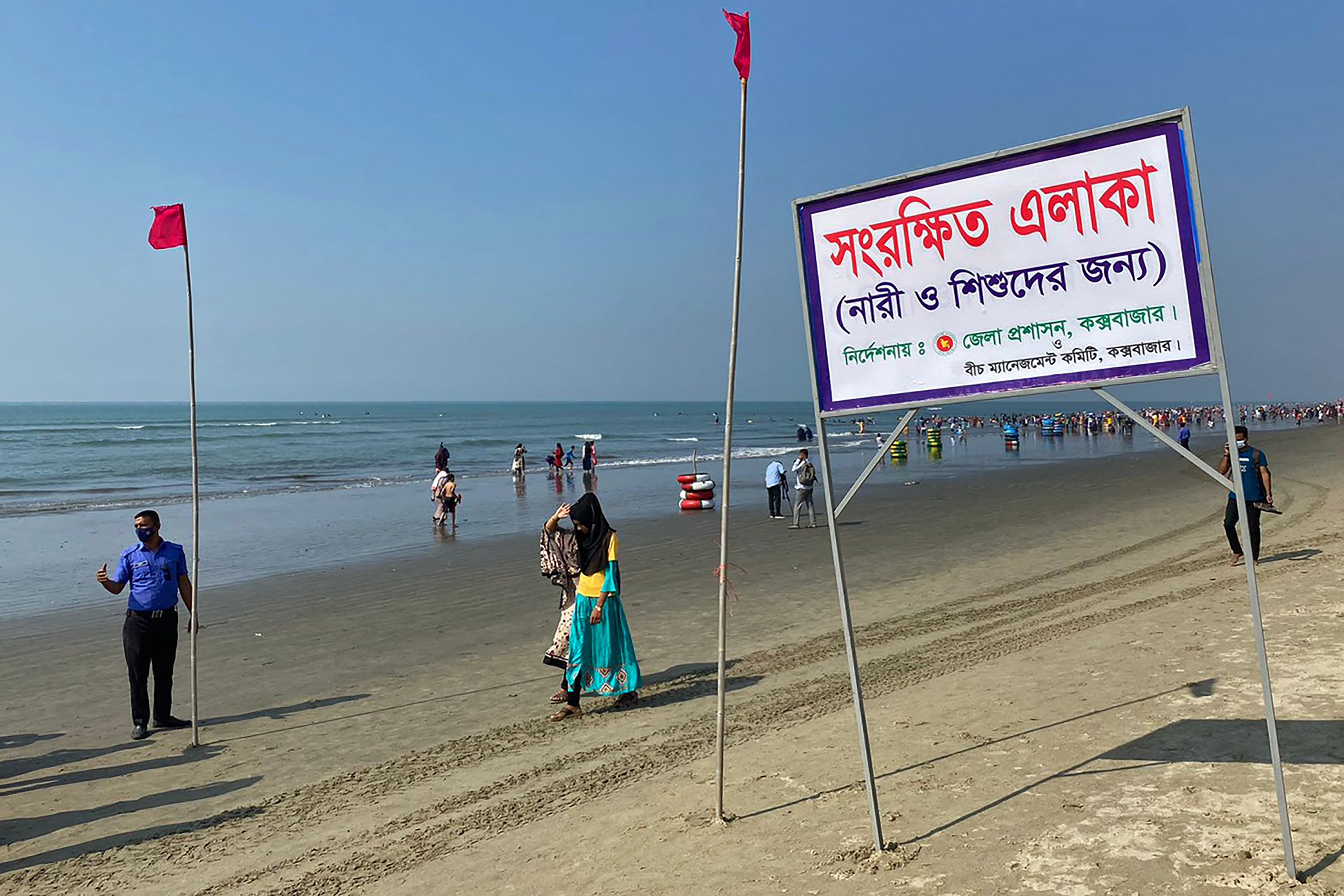 People walk past a signboard reading "Reserved area for women and children as instructed by the district commissioner" along a beach in Cox's Bazar