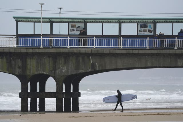 A surfer walks into the sea off Bournemouth beach in Dorset (PA)