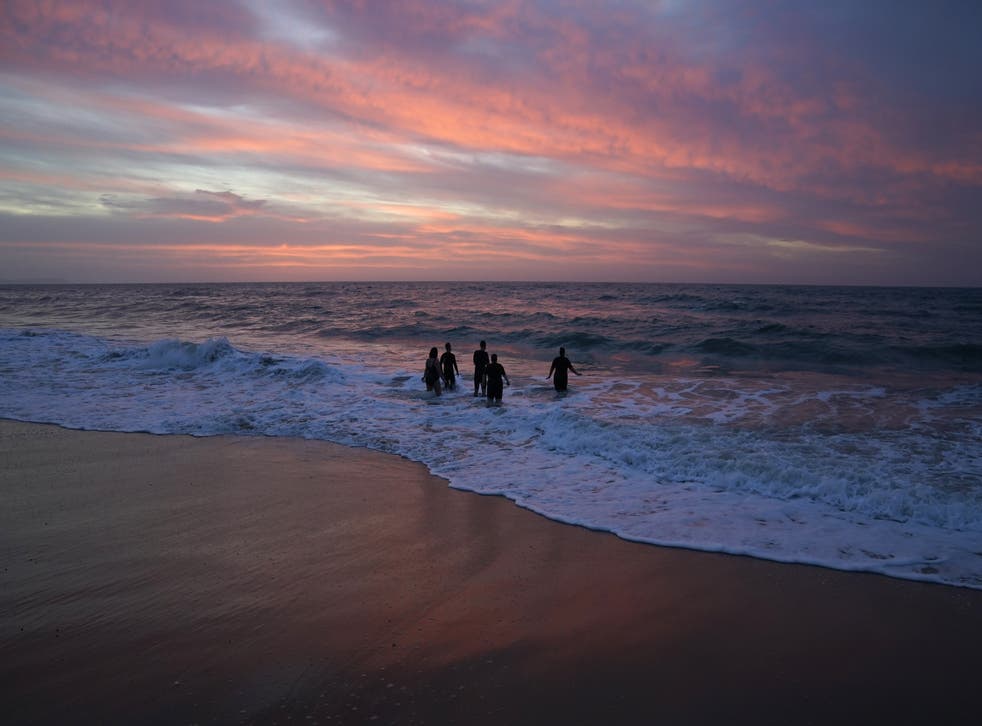 Swimmers make their way out to sea as the sun begins to rise over Boscombe beach in Dorset (Andrew Matthews/PA)