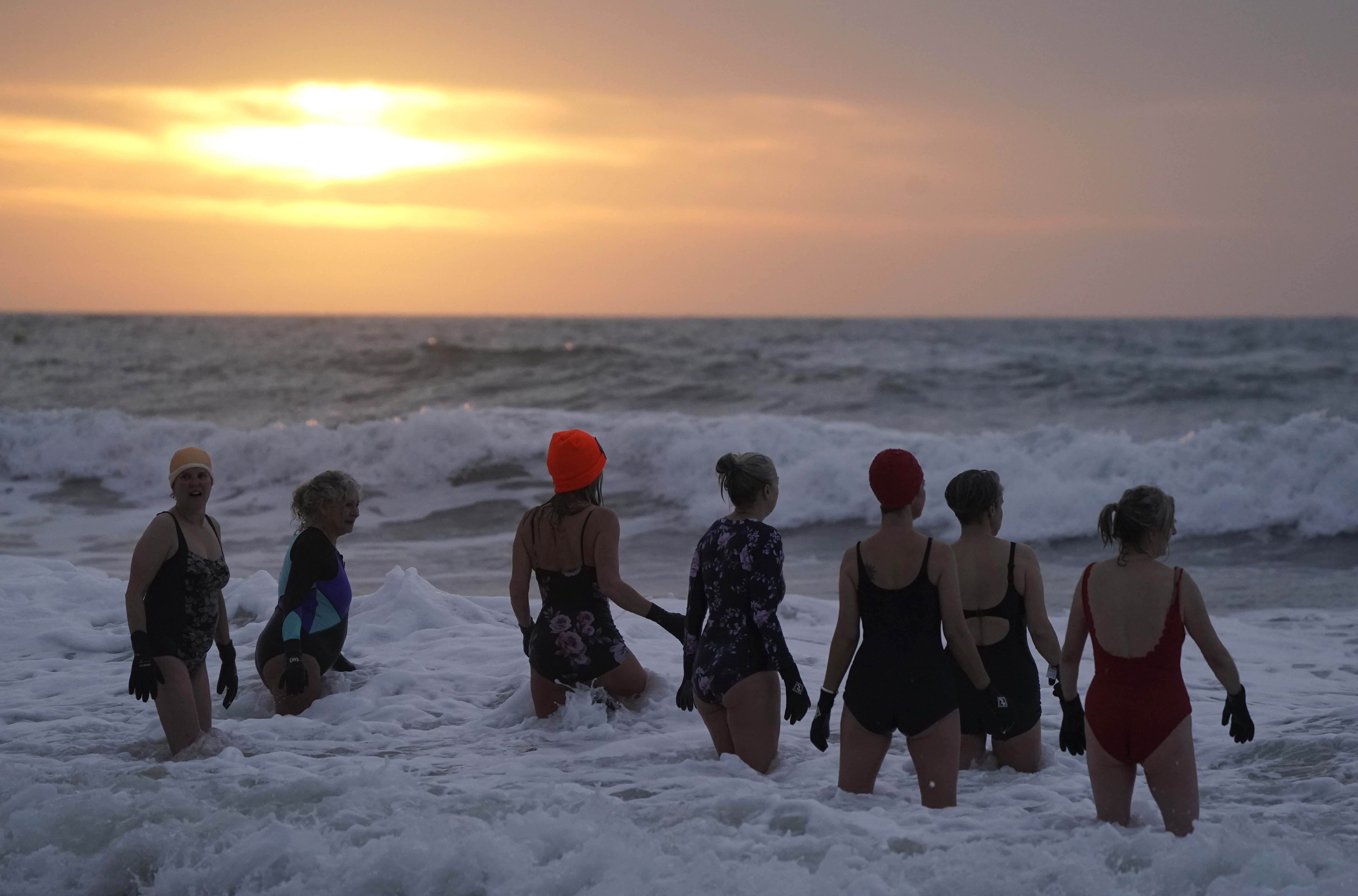 Swimmers make their way out to sea as the sun begins to rise over Boscombe beach in Dorset on New Year’s Day (Andrew Matthews/PA)