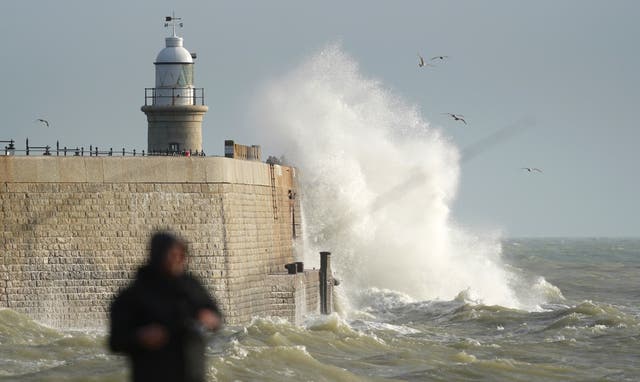 A fisherman on the beach in Folkestone, Kent, as waves crash against the harbour wall during strong winds (Gareth Fuller/PA)