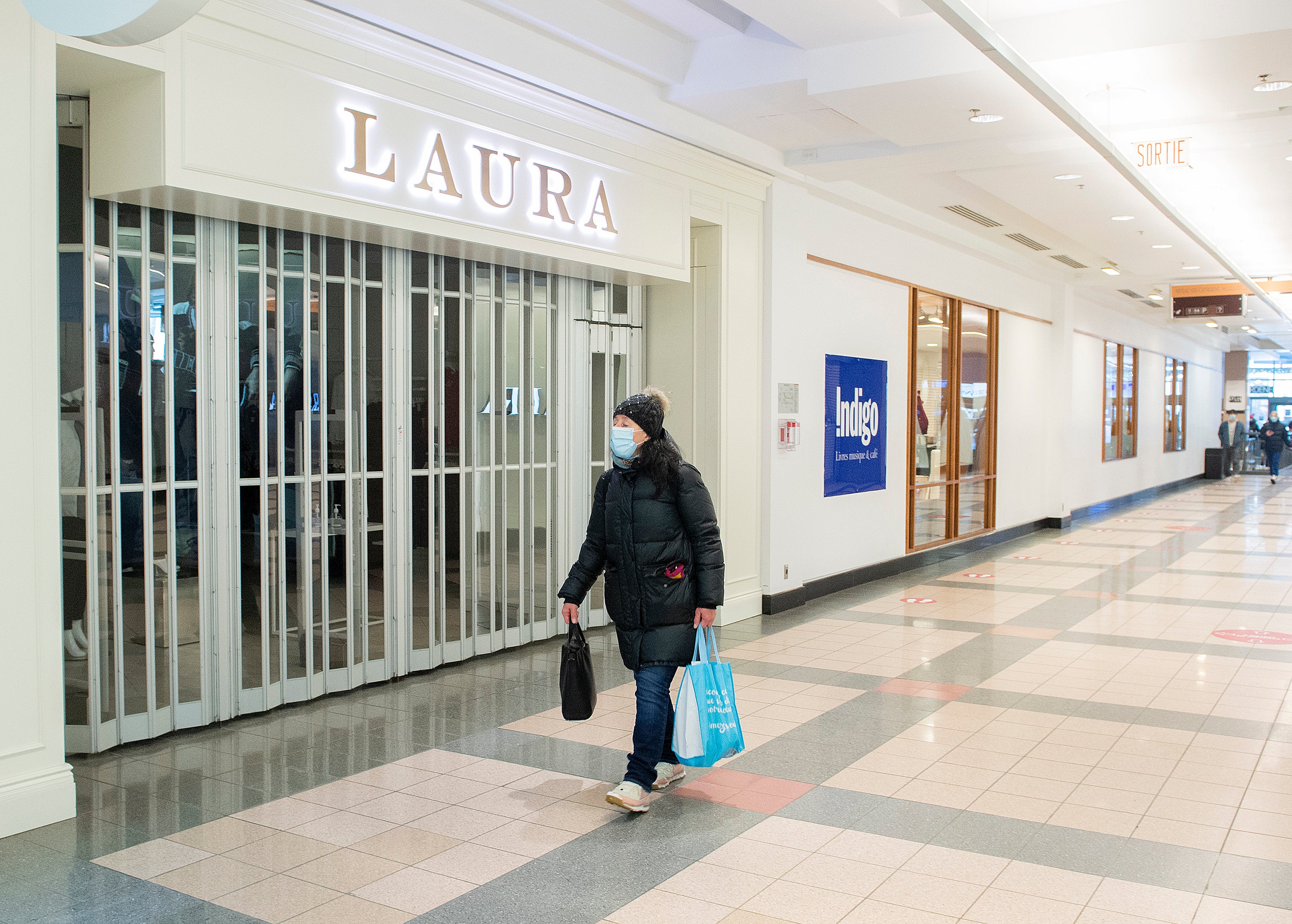 <p>A woman walks by a closed store in a mall in Montreal, Sunday, Jan. 2, 2022, as the COVID-19 pandemic continues in Canada. Some measures put in place by the Quebec government, including the closure of stores, go into effect today to help curb the spread of COVID-19 in the province.  (Graham Hughes /The Canadian Press via AP)</p>