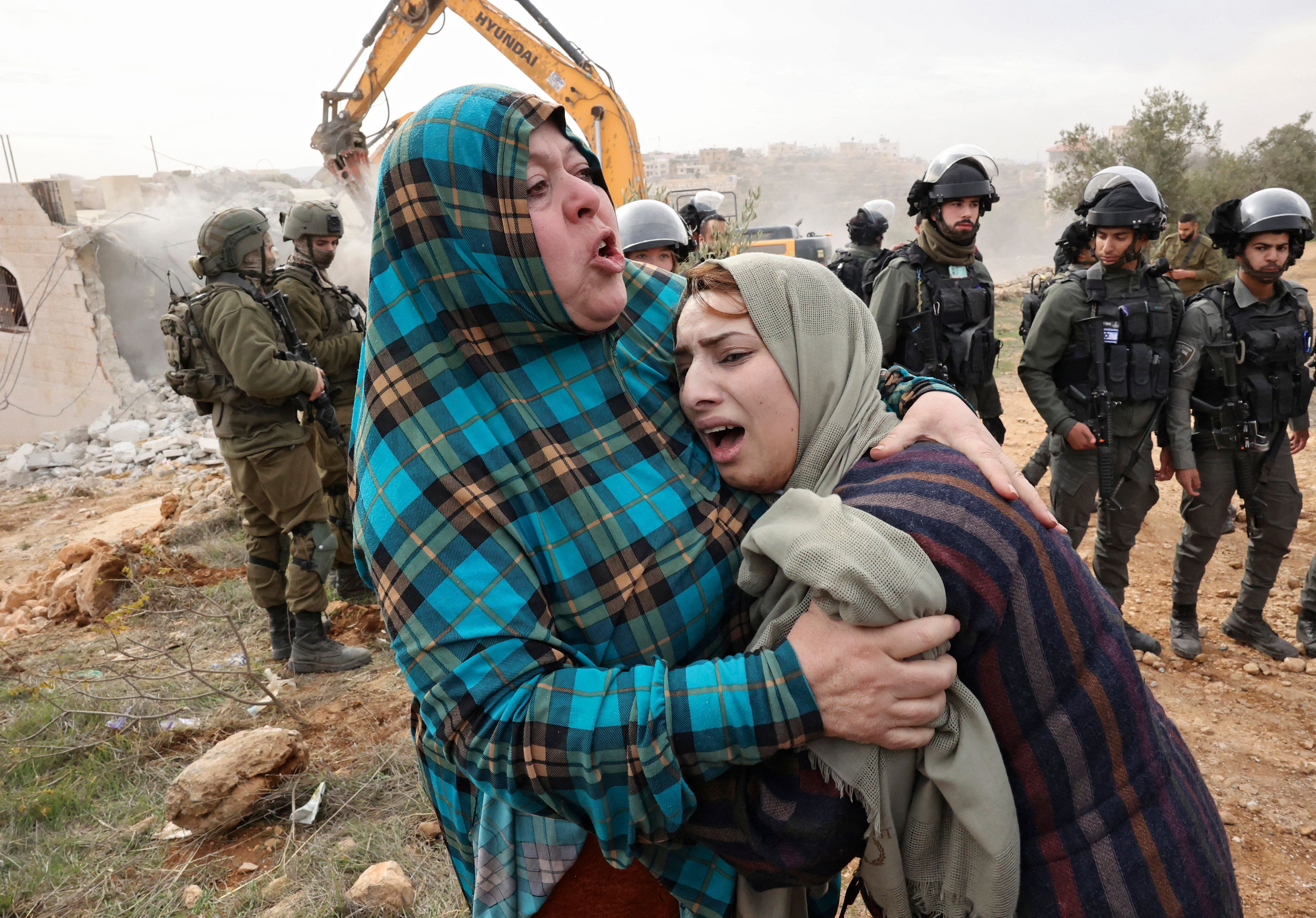 Israeli forces stand guard as Palestinian women react to the demolition of their home in the occupied West Bank town of Hebron on 28 December 2021