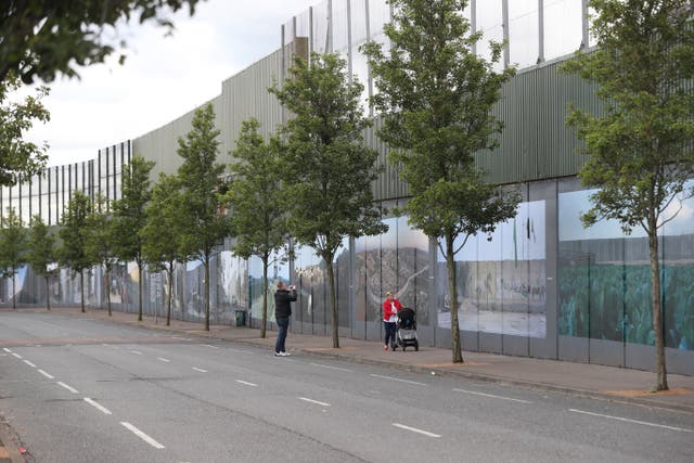 People walk past a peace wall between the Falls Road and Shankill Road in west Belfast (Niall Carson/PA)