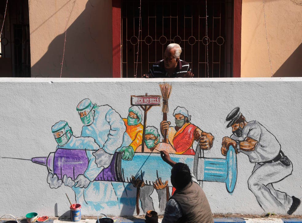 <p>An artist gives his finishing touches to a mural depicting frontline workers carrying a Covid vaccine in Kolkata on 2 January 2021</p>