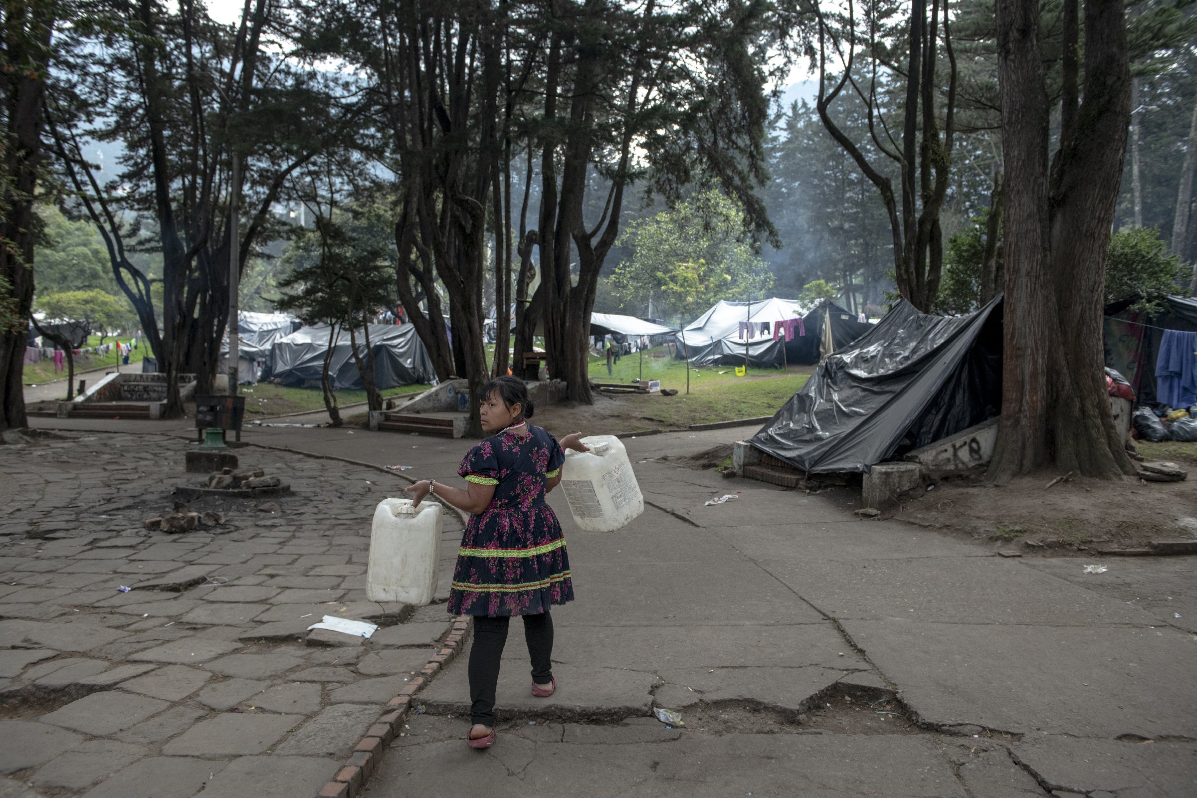 Maria Lubia Queracama Tanigama carries two cans to fill at the spring that provides water for the protest camp in National Park in the centre of Bogota