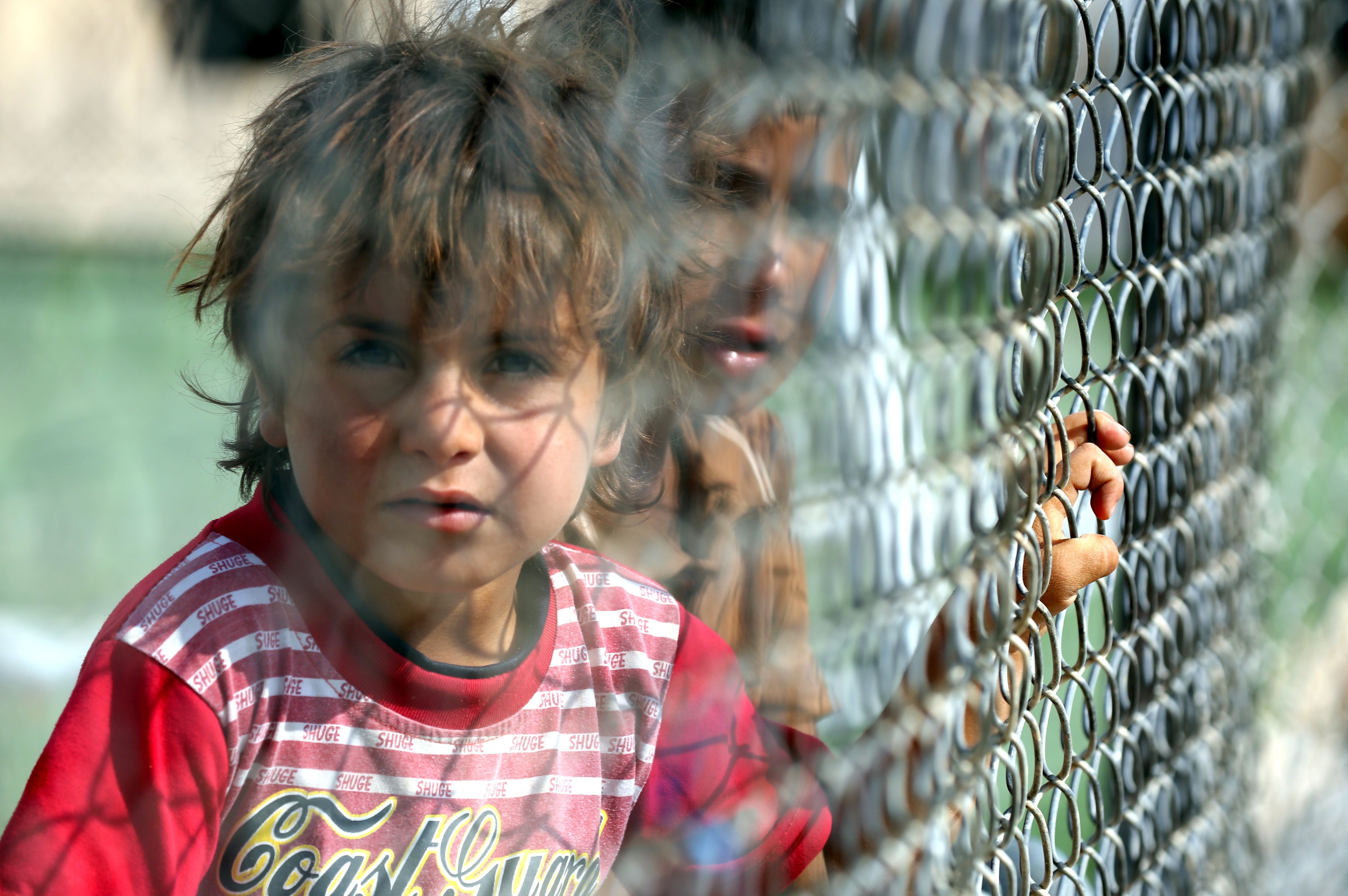 Iraqi children look from behind a fence at the Al-Hol refugee camp in Syria