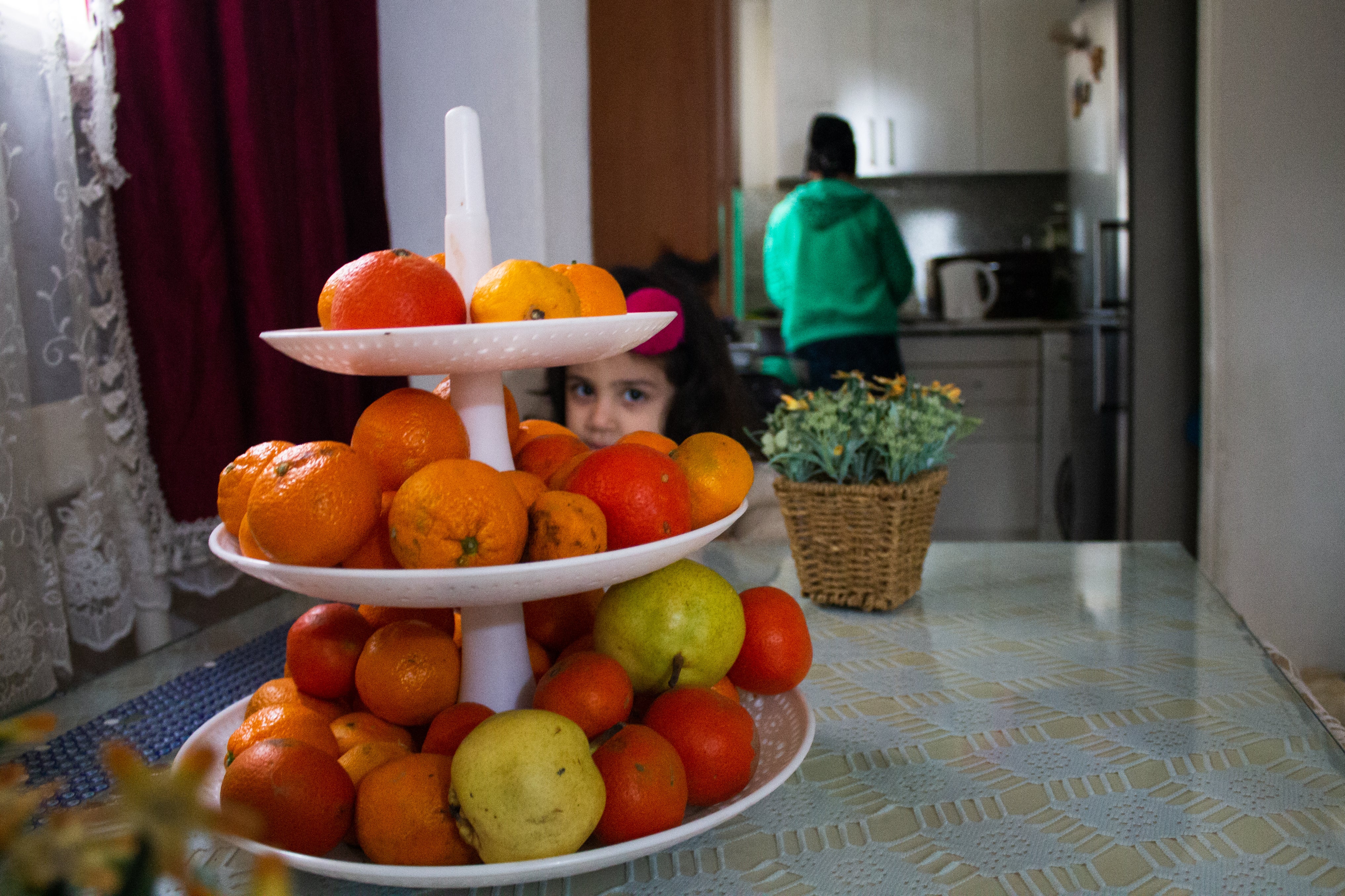 Yasemin Tekin in the kitchen while her daughter peers through plates of fruit. The family struggle to make ends meet