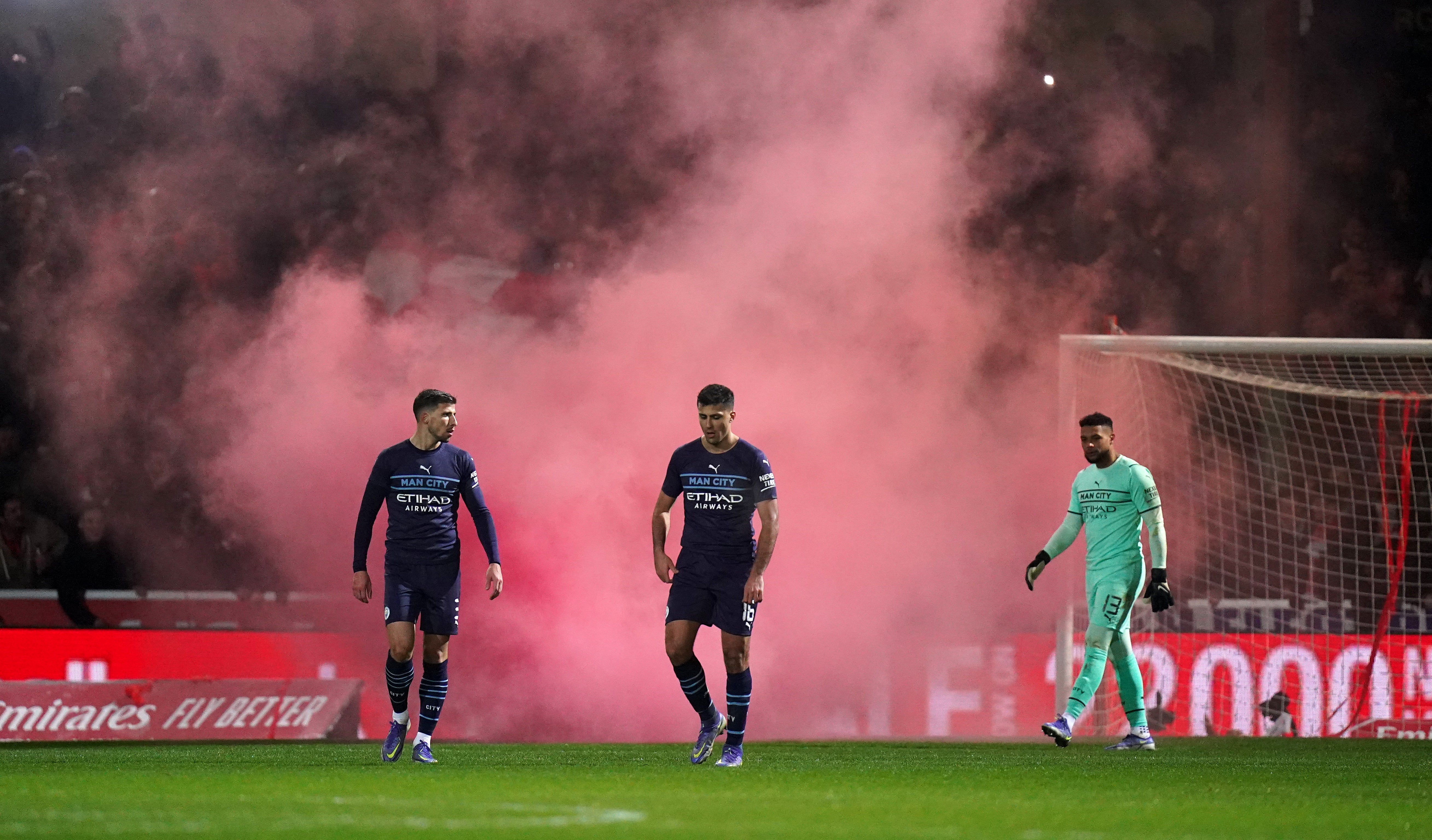 Manchester City’s Ruben Dias (left), Rodri (centre) and Zack Steffen look on as Swindon fans set off a smoke flare (PA Images/Adam Davy)