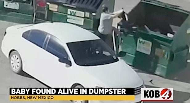 Woman is seen tossing a black trash bag into a dumpster