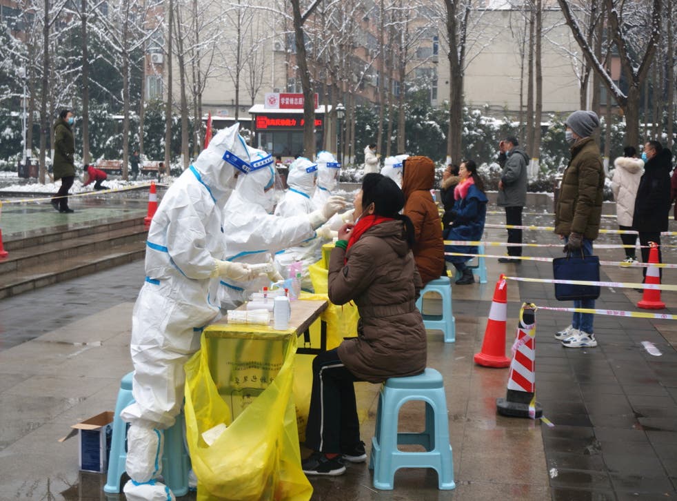 <p>Medical workers in protective suits collect swabs from residents during a citywide nucleic acid testing following Covid cases in Zhengzhou city in China’s Henan province on 5 January 2022 </p>