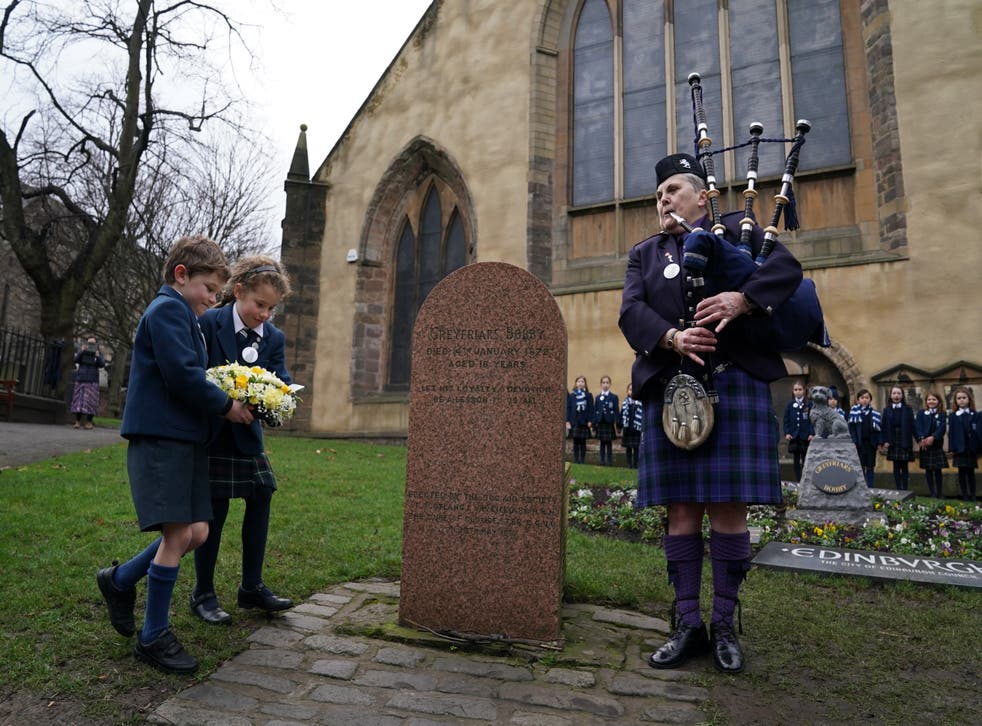 Piper Jennifer Hutcheon plays as pupils Arthur Rudd and Imogen Piper lay flowers at the graveside (Andrew Milligan/PA)