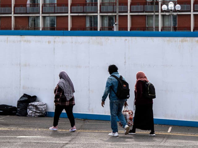 <p>Asylum seekers enter the Crowne Plaza hotel in London through an exterior perimeter wall that was installed during their stay in February </p>