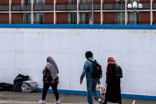 <p>Asylum seekers enter the Crowne Plaza hotel in London through an exterior perimeter wall that was installed during their stay in February </p>