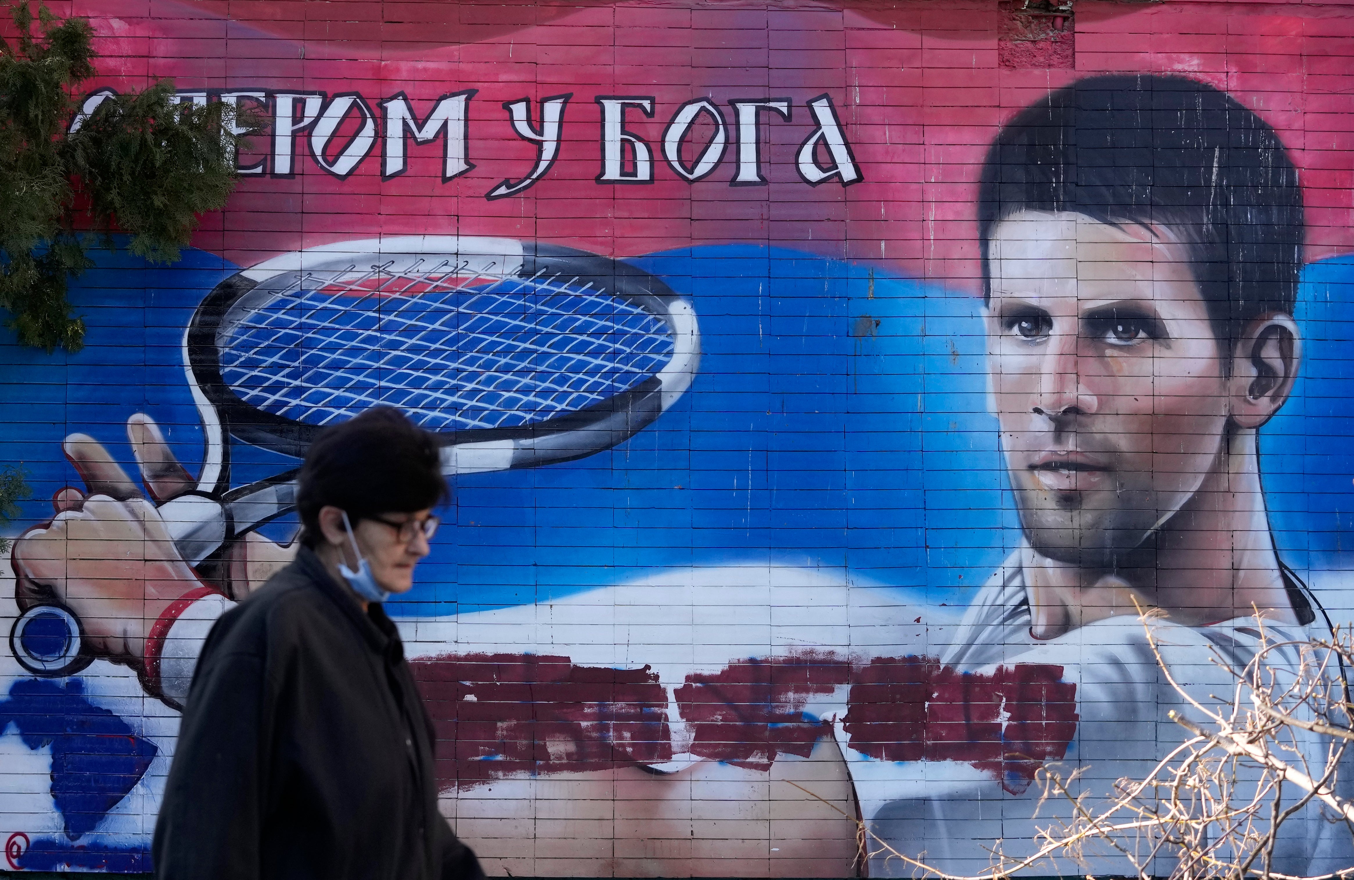 A woman passes a mural depicting Serbian tennis player Novak Djokovic, reading: “With faith in God” on a wall in Belgrade. Djokovic was deported from Australia on Sunday after failing to overturn the decision to cancel his visa (Darko Vojinovic/AP)