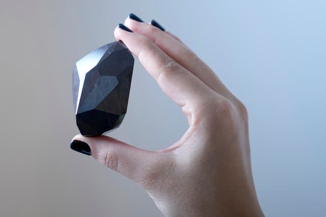 <p>An employee of Sotheby's Dubai presents a 555.55 Carat Black Diamond "The Enigma" </p>