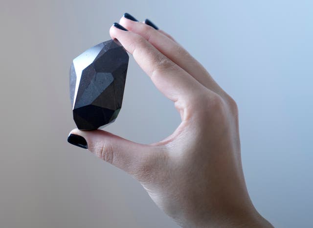 <p>An employee of Sotheby's Dubai presents a 555.55 Carat Black Diamond "The Enigma" </p>