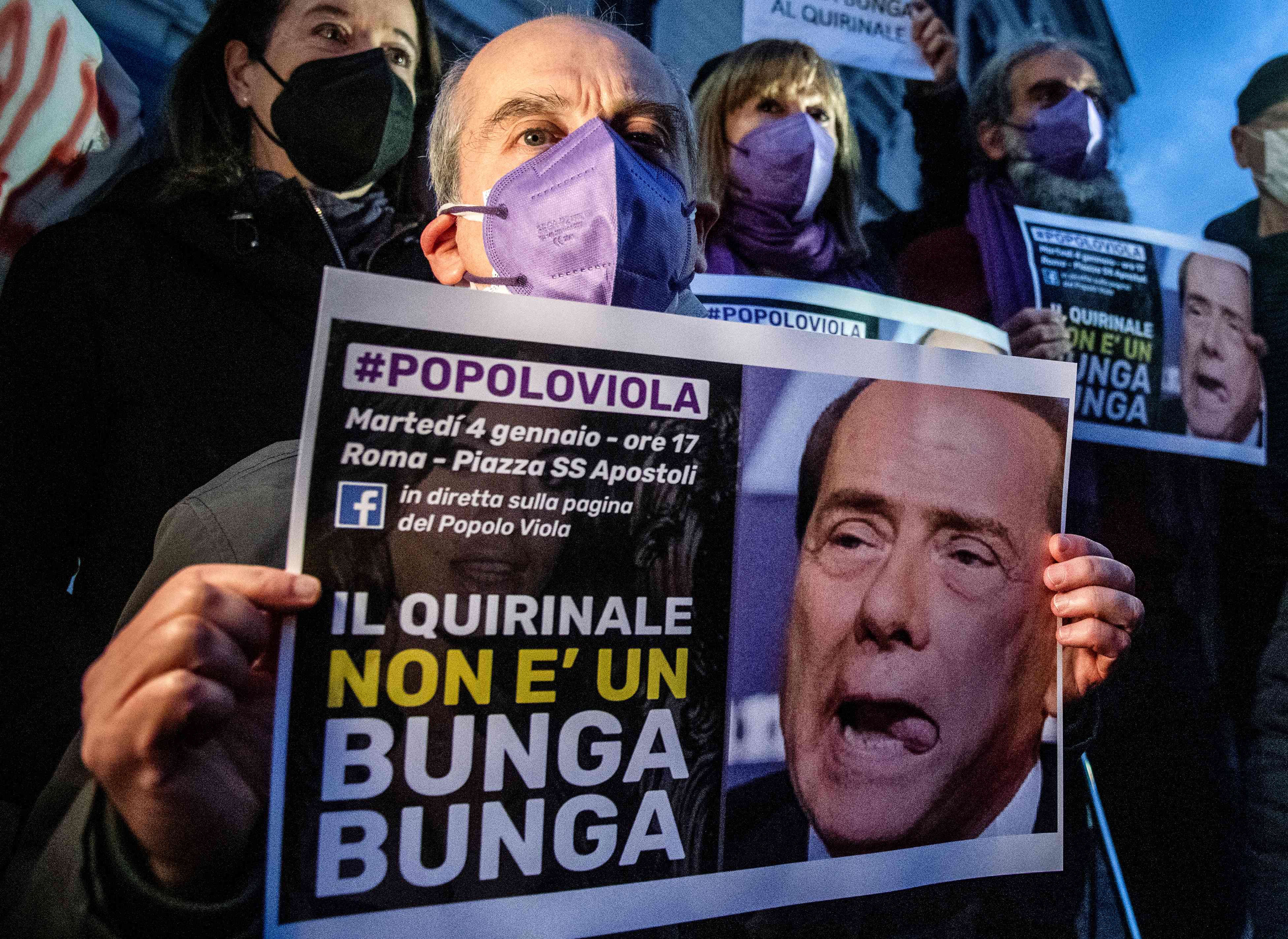 A man holds a poster depicting Silvio Berlusconi that reads ‘The Quirinale is not a Bunga Bunga’ during a protest in Rome in January