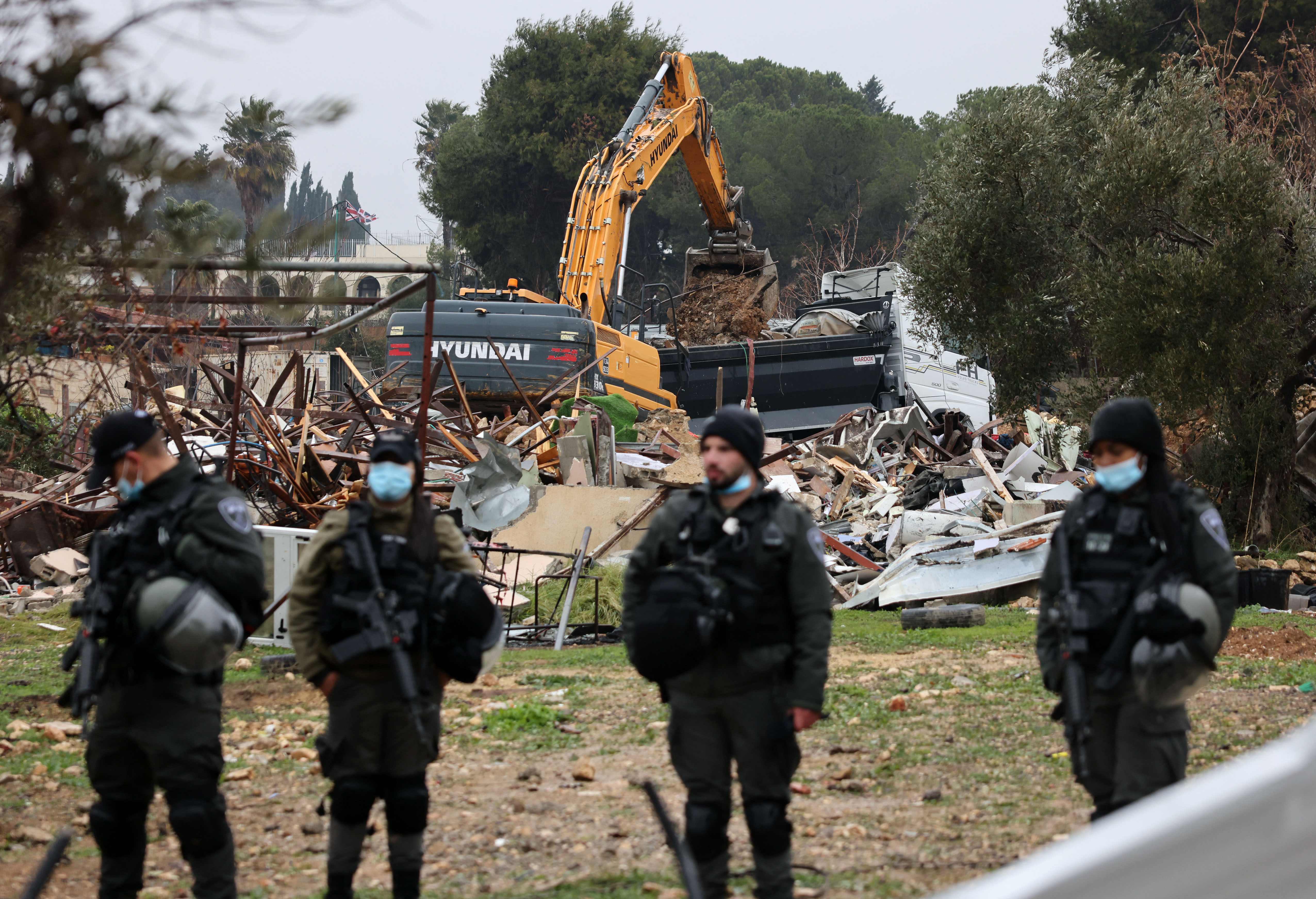 Israeli forces stand guard as machinery clean the ruins of the Palestinian Salhiya family’s house, in the Sheikh Jarrah neighbourhood