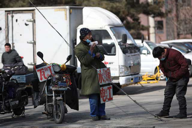 <p>File photo: A migrant worker stands with signs advertising his work skills on a street as he waits to get hired in Shenyang, China, 25 February 2021</p>