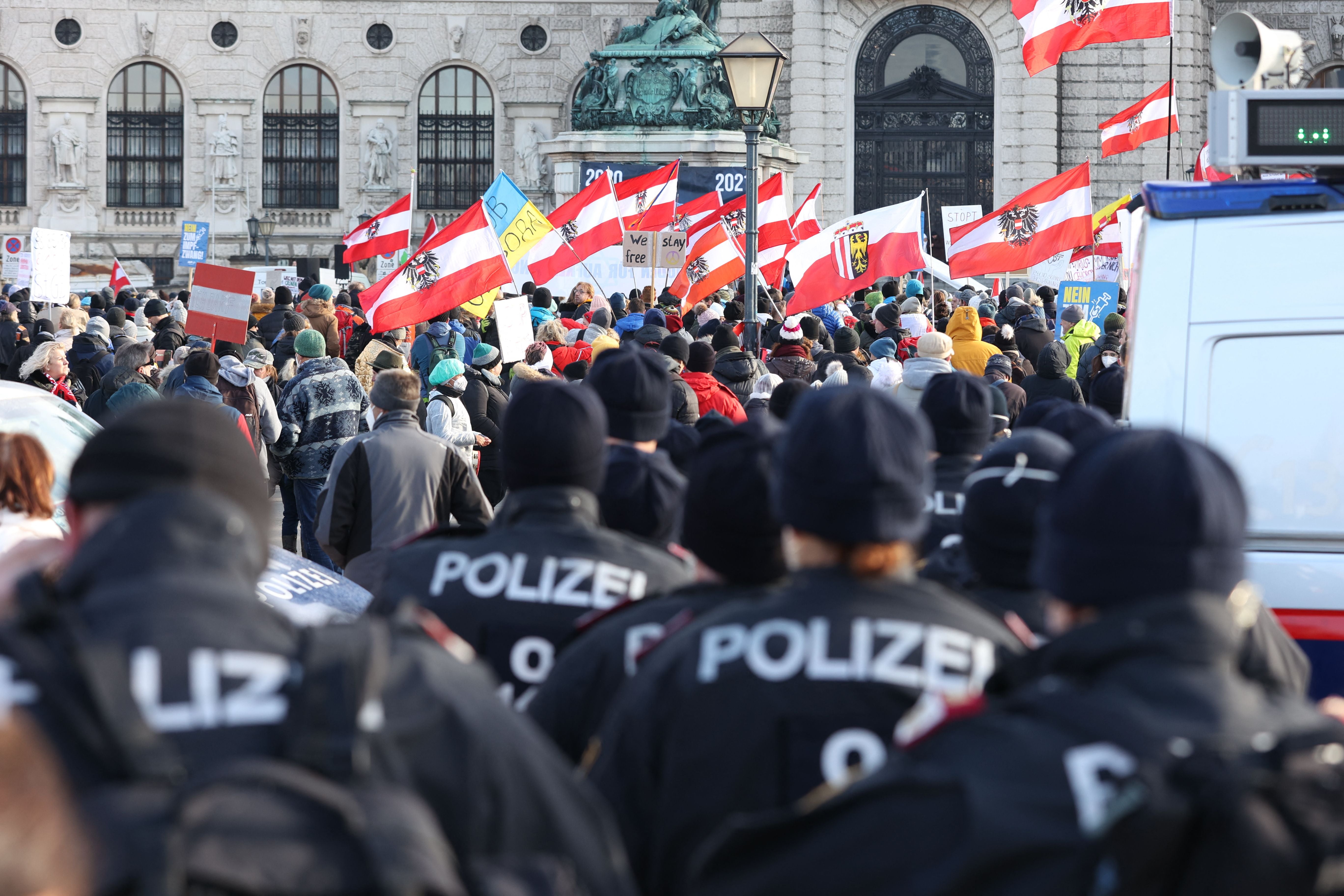 Policemen look on as people carry Austrian flags as they demonstrate in Vienna on 8 January 2022