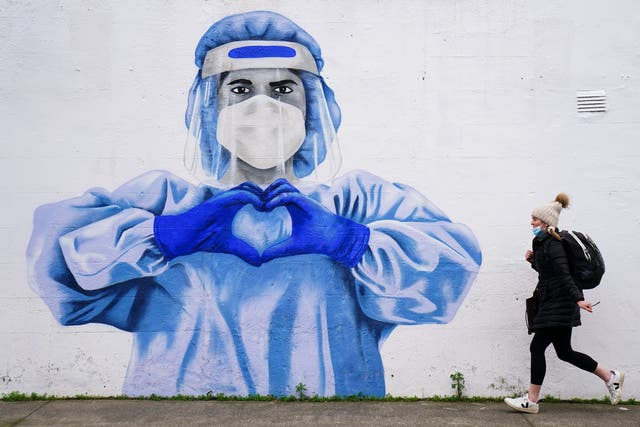 A woman passes a mural of a frontline worker in Dublin (PA)