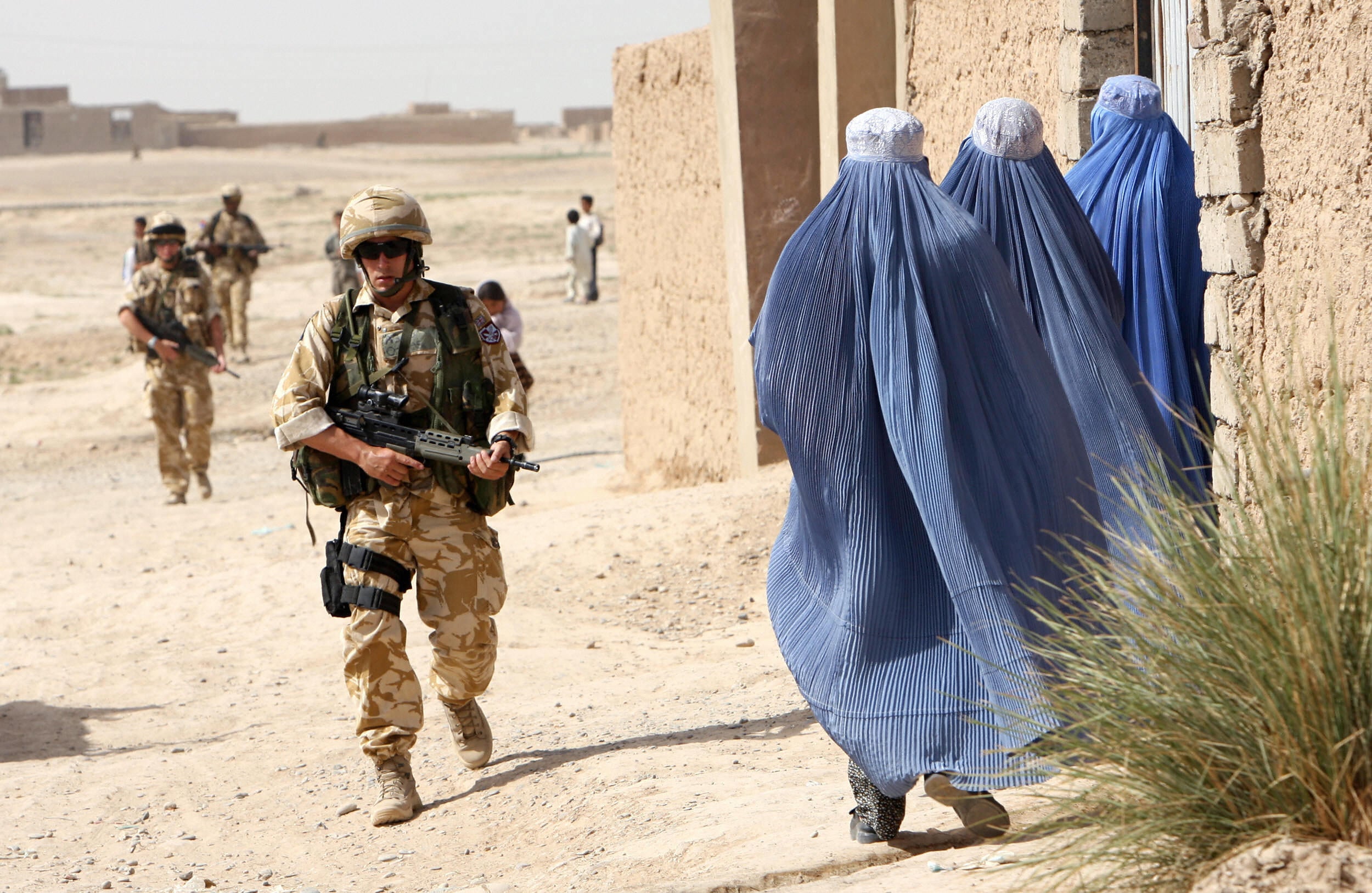 A British soldier from 16 Air Assault Brigade walks past three women wearing burkas during a foot patrol in Helmand province, in 2006