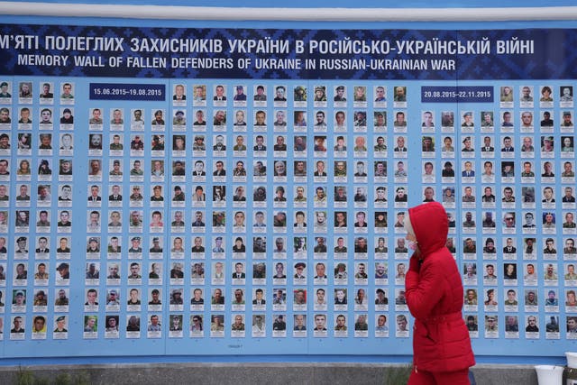 Una mujer pasa junto al Muro del Recuerdo, que muestra las fotografías, los nombres y las fechas de nacimiento y muerte de aproximadamente 4500 soldados profesionales y voluntarios que han muerto luchando por Ucrania en el actual conflicto de Donbass.